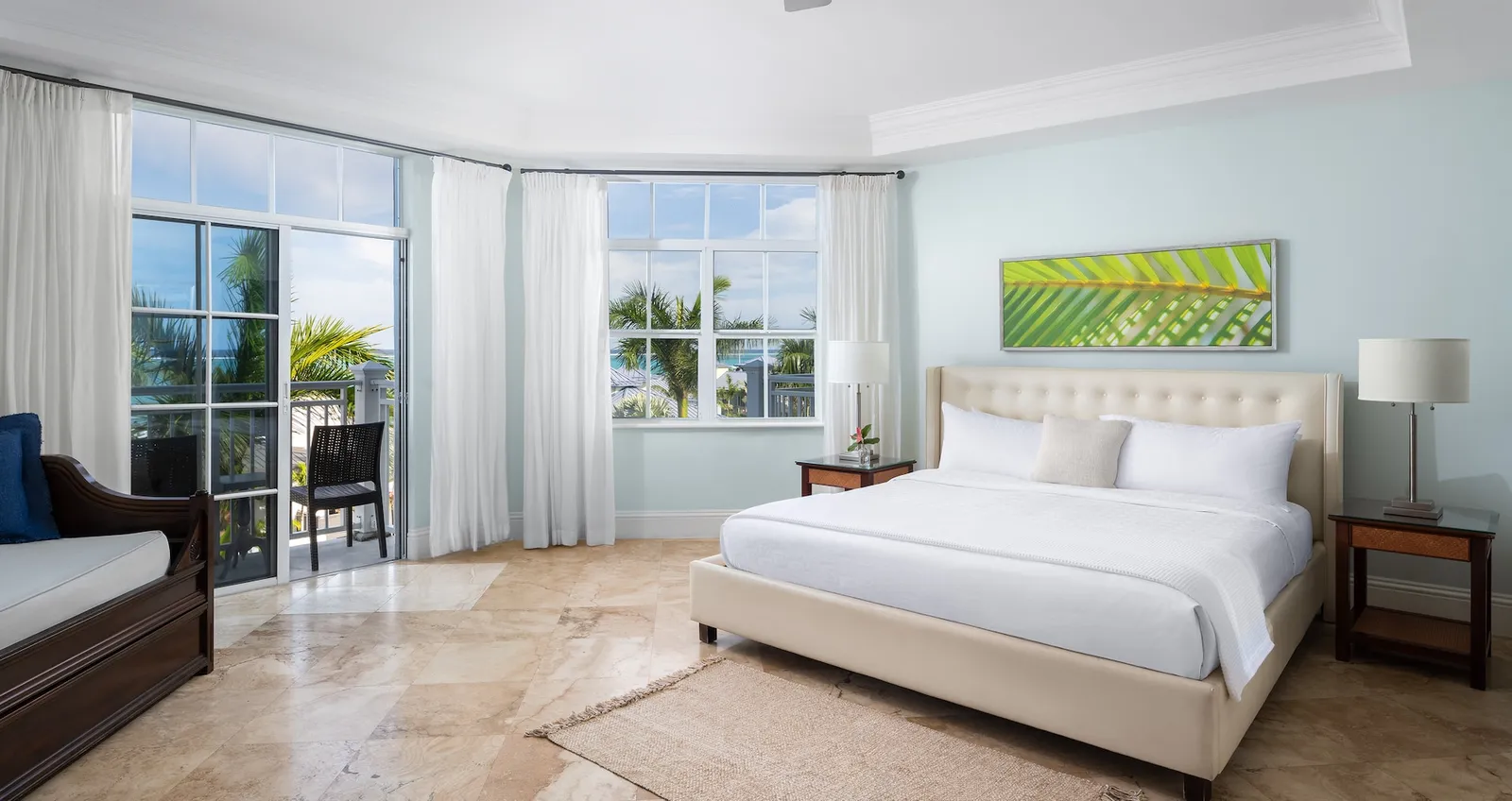 A bright corner room: a king bed with a cream headboard, a daybed, a marble floor and the doors to the balcony.