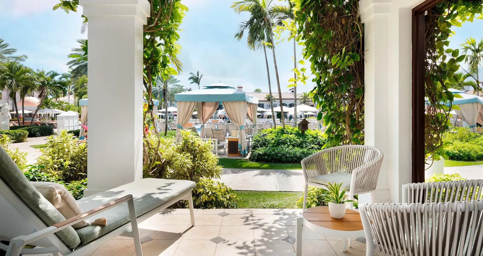 A ground-floor terrace between columns and climbing plants, with loungers and a view of the pool’s cabanas.