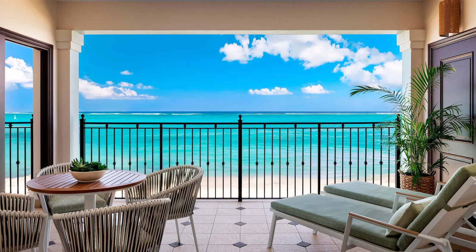 A covered balcony facing the beach and the turquoise sea, with a round table, chairs and 2 loungers.