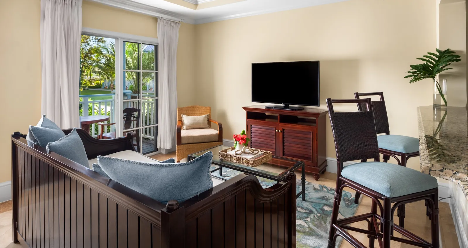 A living room with a daybed and blue cushions, the television cabinet, tall stools and the door to the balcony.