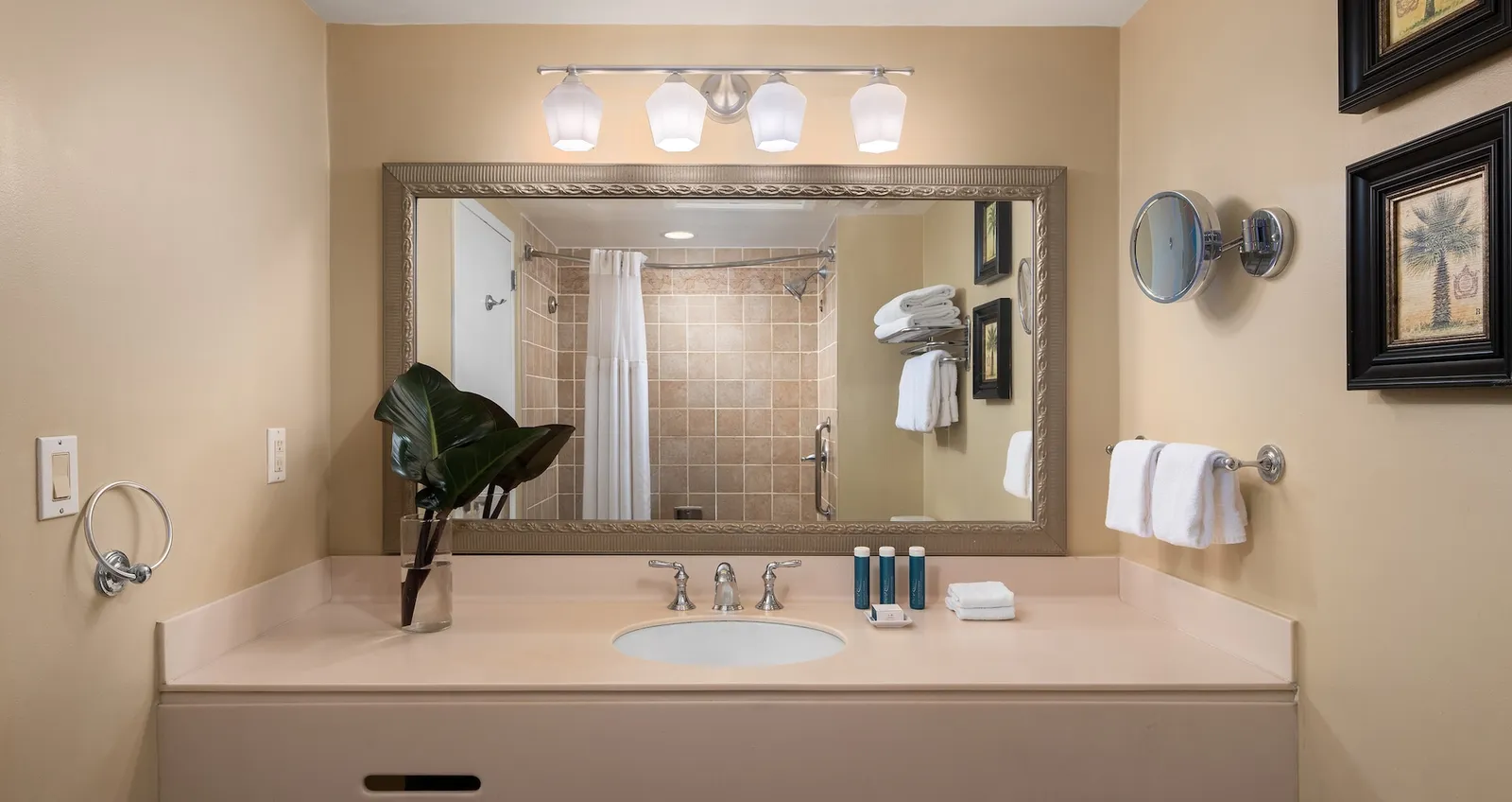 The bathroom: a sand-coloured basin under a framed mirror, white towels and the shower in the reflection.