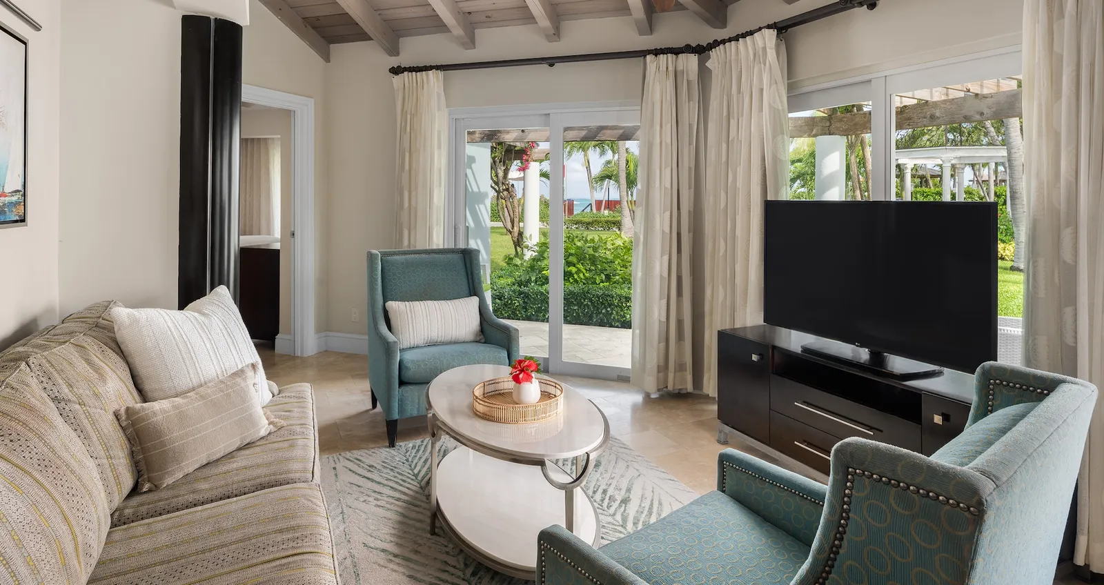 A living room with a beige sofa, 2 teal armchairs, an oval coffee table and sliding doors to the garden.
