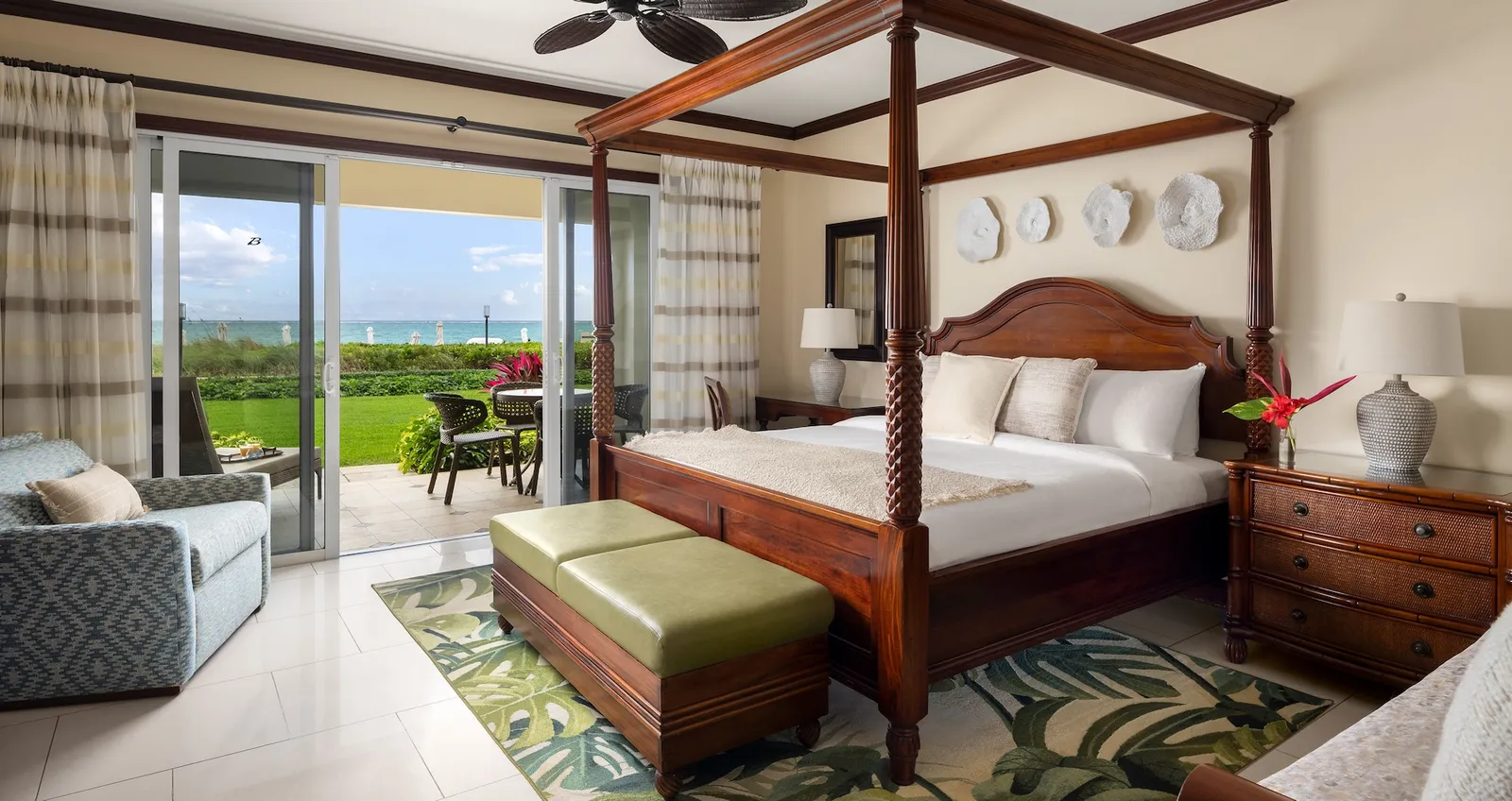 A four-poster king bed and, beyond the open sliding door, the patio, the lawn and the sea.