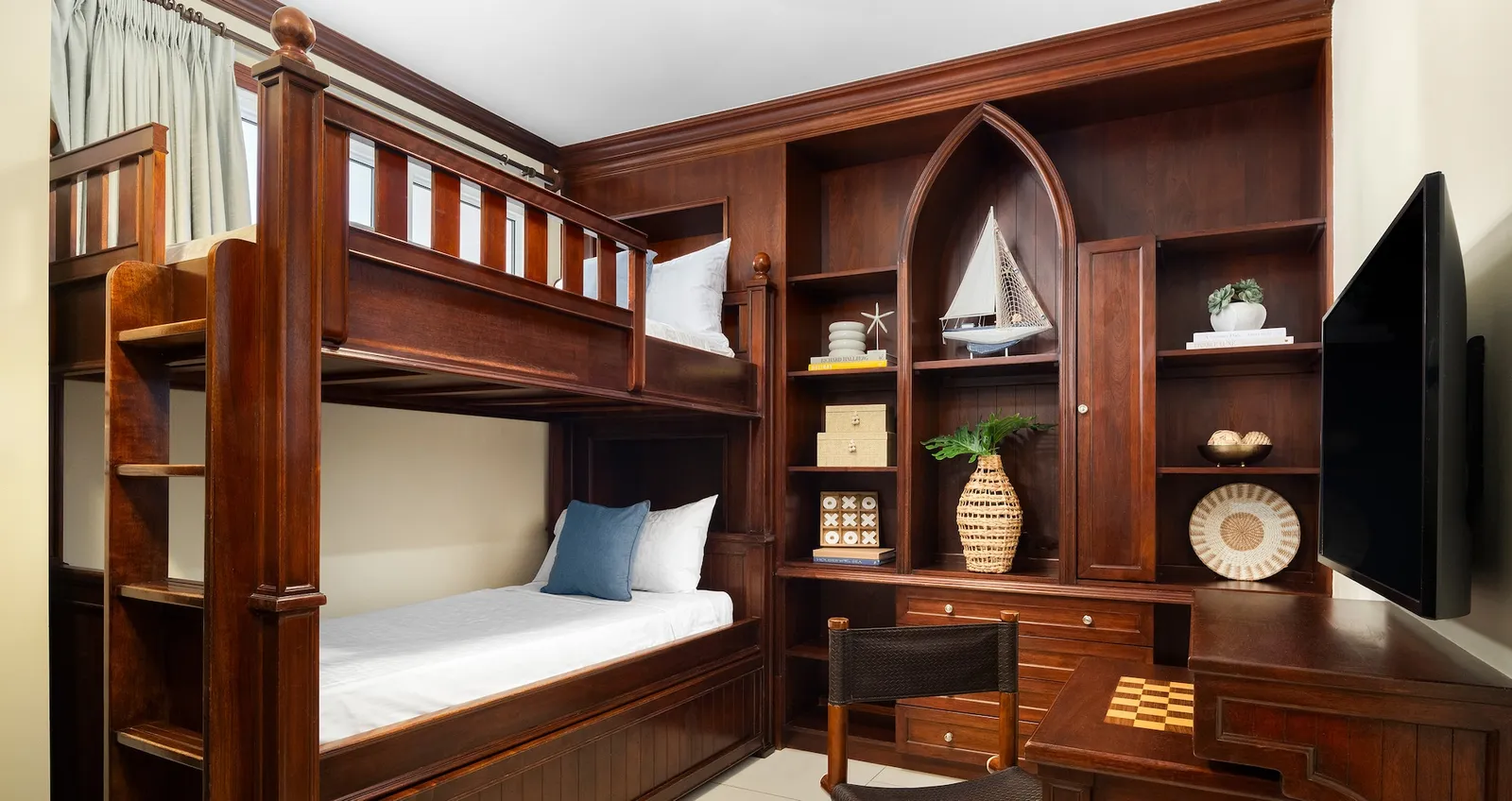 The children’s room: a mahogany bunk bed, a built-in wall unit with a model sailing boat, the television and a small desk.