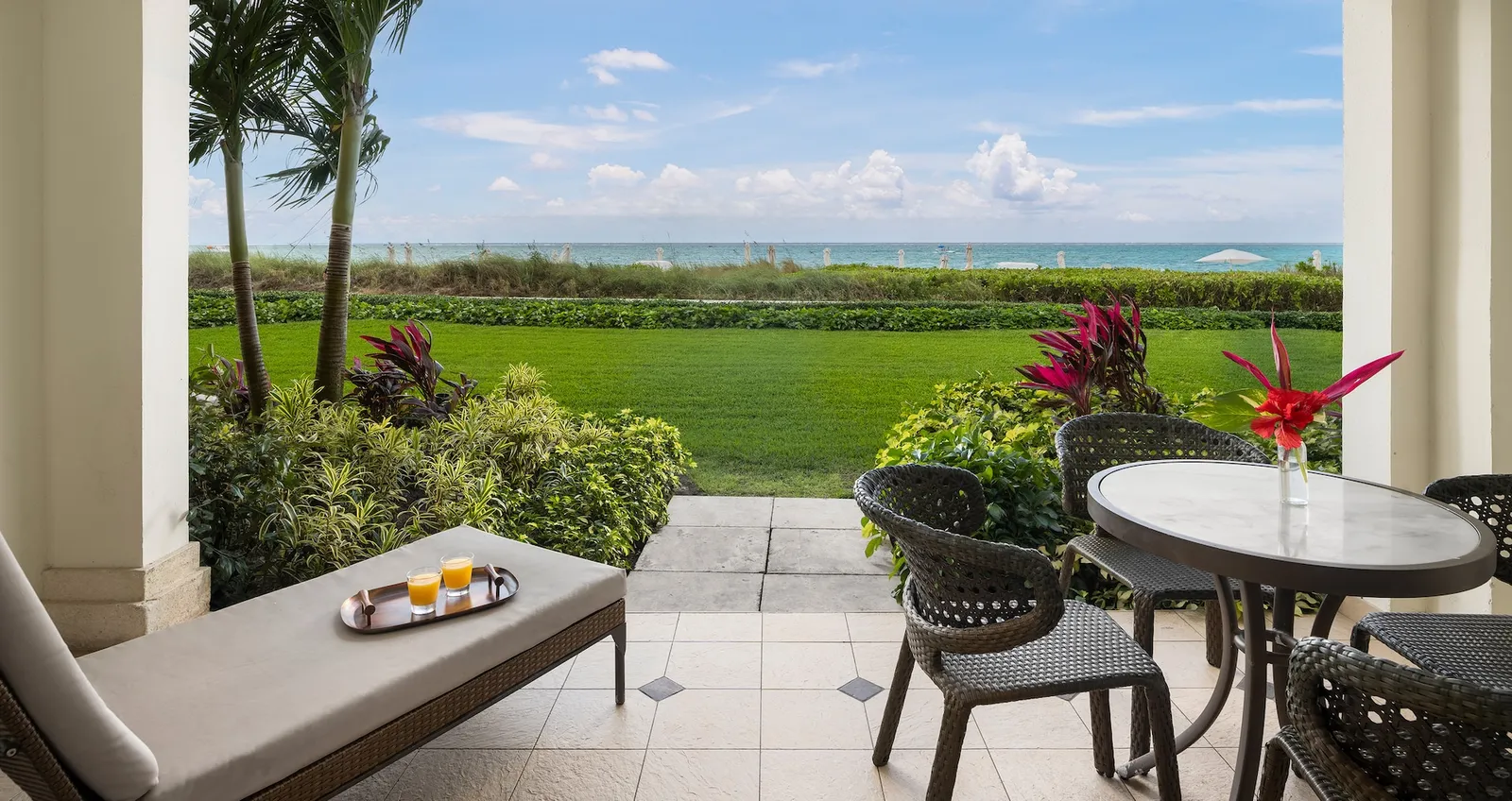 A ground-floor patio with a table, chairs and a lounger, and the lawn running down to the dune and the sea.