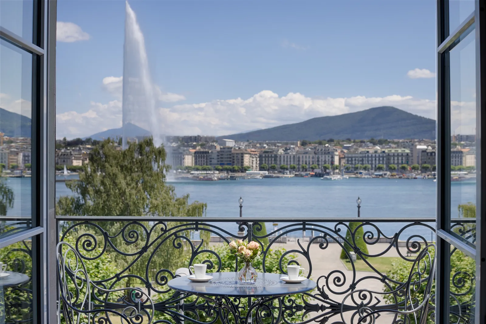 Una porta-finestra aperta sul balcone, con il lago e il Jet d’Eau