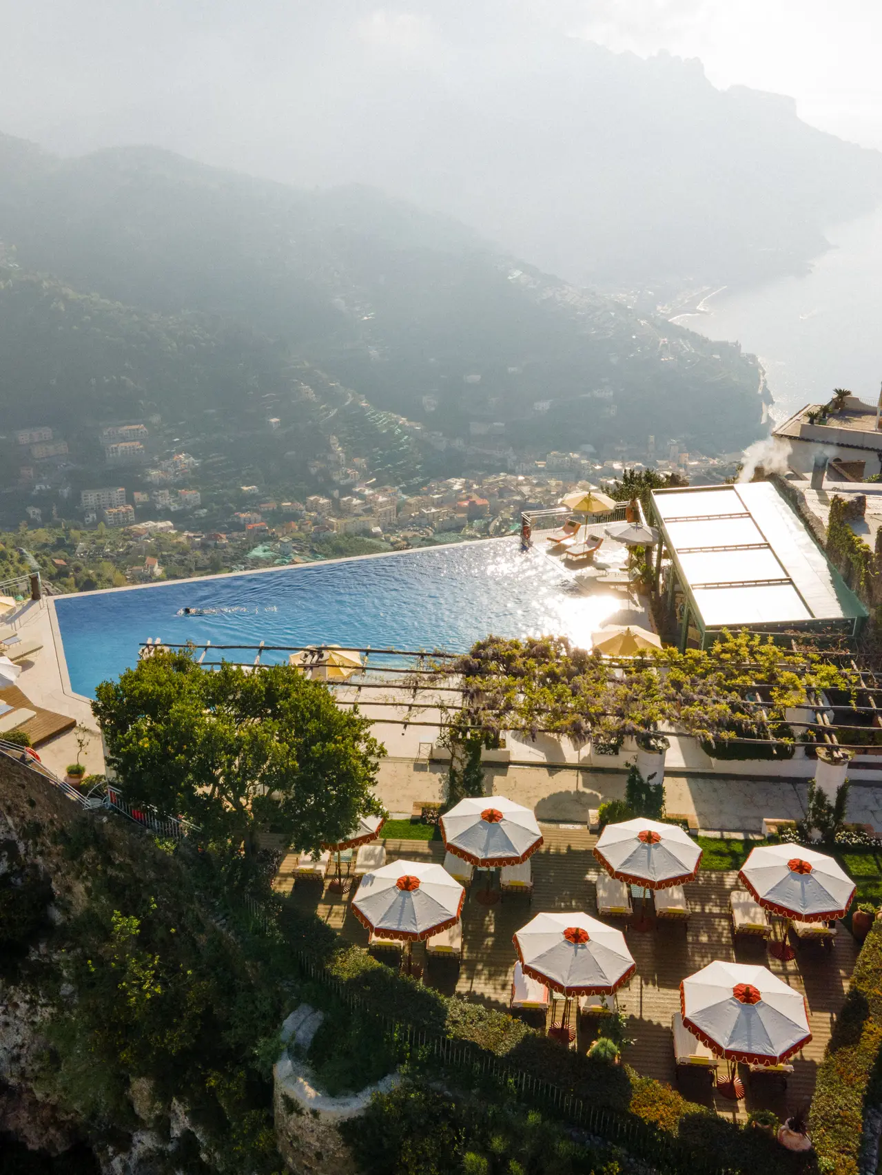 The pool and the terraces with their parasols seen from above, on the edge of the slope, the coast in the haze.