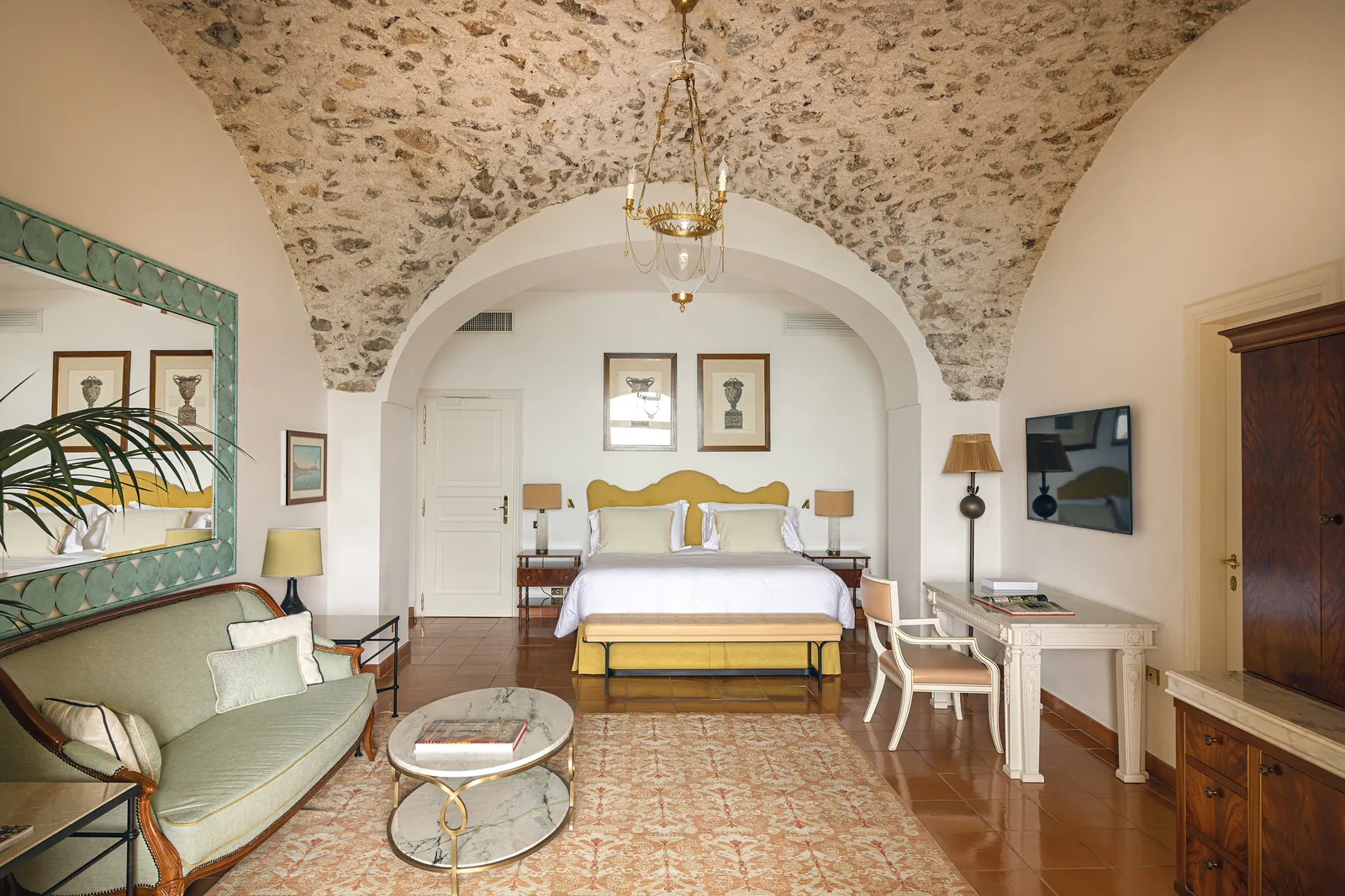 A Deluxe Sea View Room with Balcony under a bare stone vault: the bed with its yellow headboard, a green sofa and the desk.