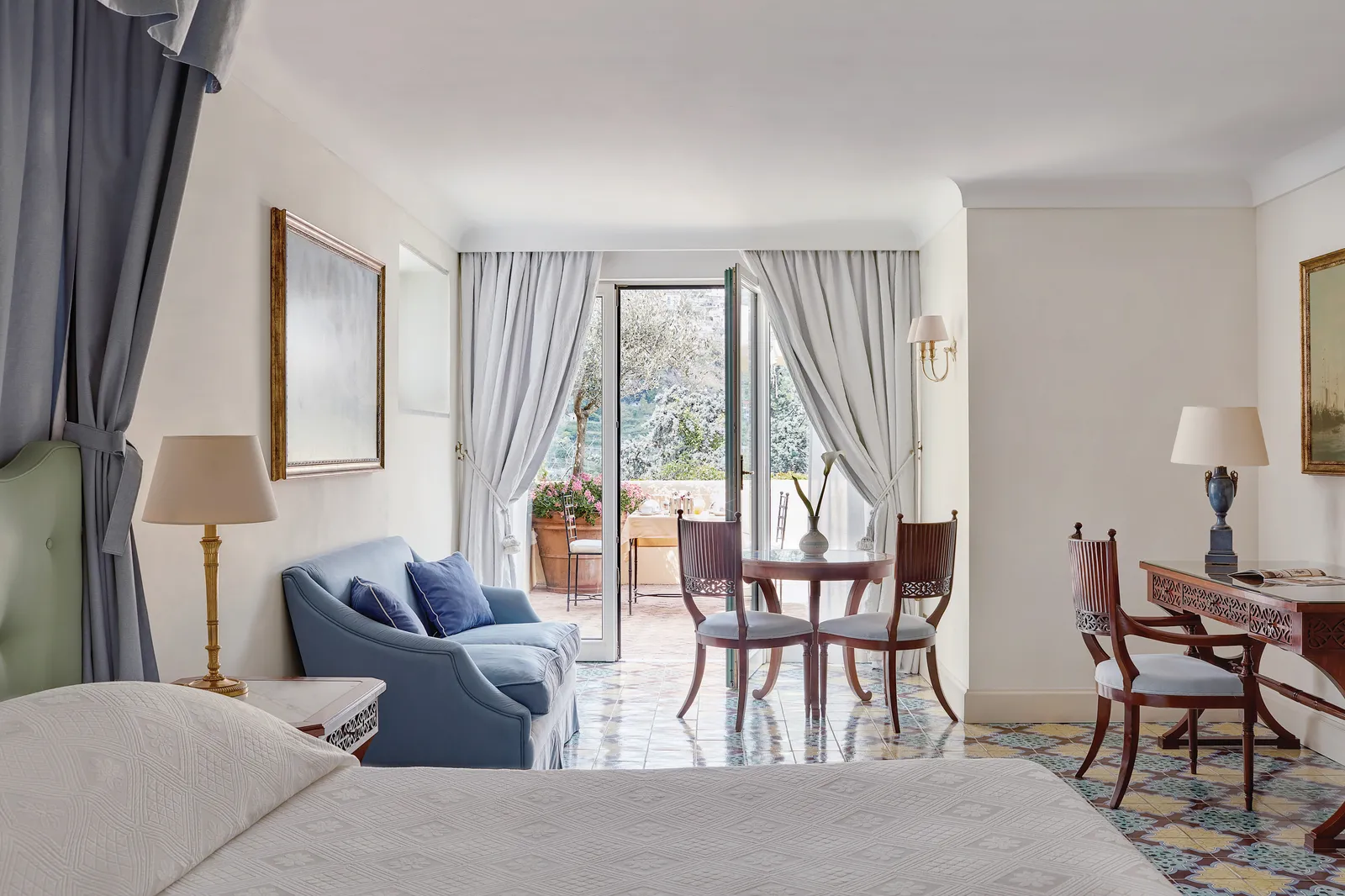 A Garden View with Terrace room: the bed, a pale blue sofa, the desk and the French window onto the terrace.