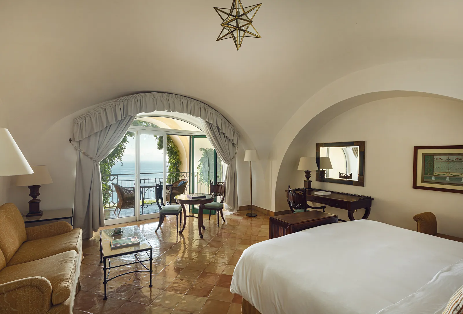 A Premium Sea View Junior Suite with Terrace: the bed, the desk and the curtained arch leading to the terrace and the sea.