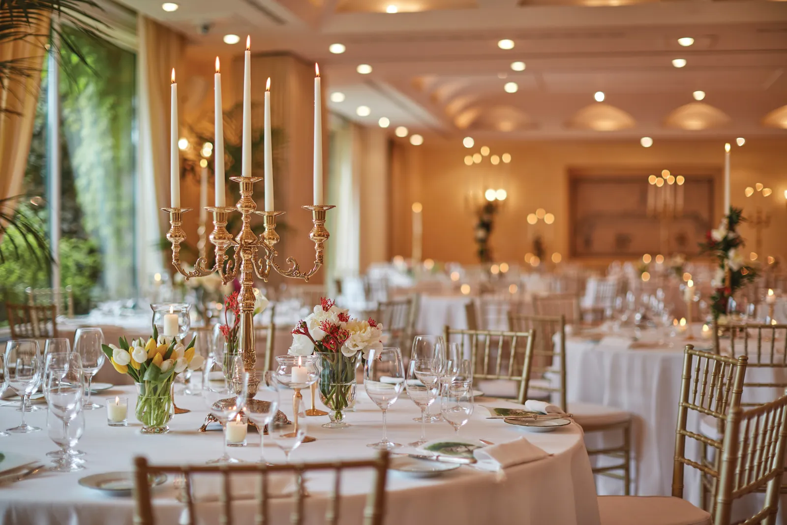 A hall laid for a banquet: round tables, gilded candelabra and gilt chairs.