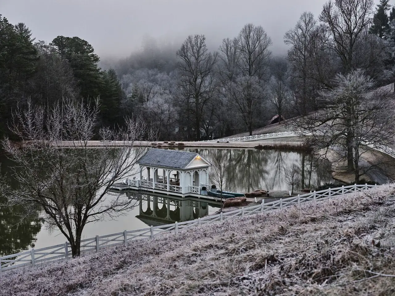 The pond and the white boathouse on a frosty morning, the trees white with rime and mist over the hills.