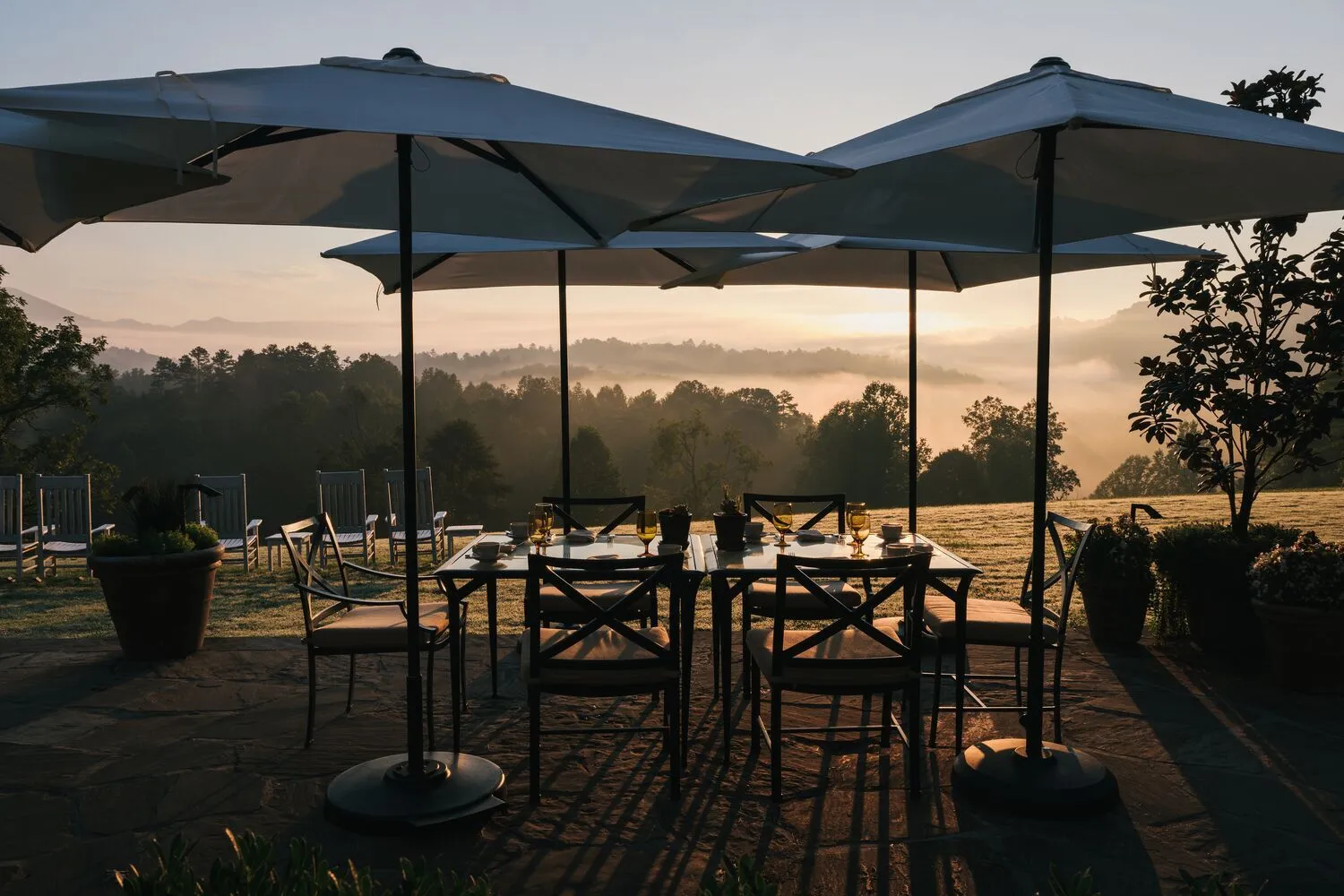 The stone terrace with its tables and parasols at sunrise, and mist in the valley below the mountain ridges.