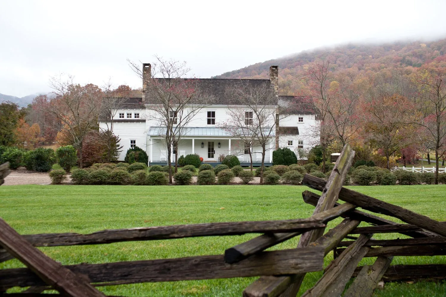 The white Farm House behind a split-rail fence, with the lawn in front and the autumn hills under low cloud.