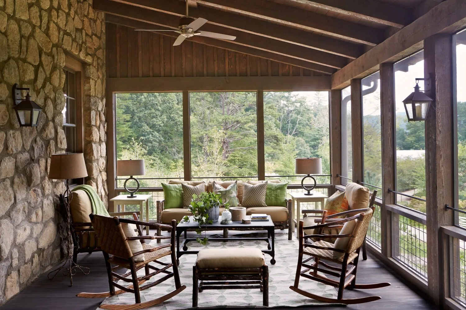 The Garden House’s screened porch, with its stone wall, sofas and rocking chairs and the green beyond the windows.