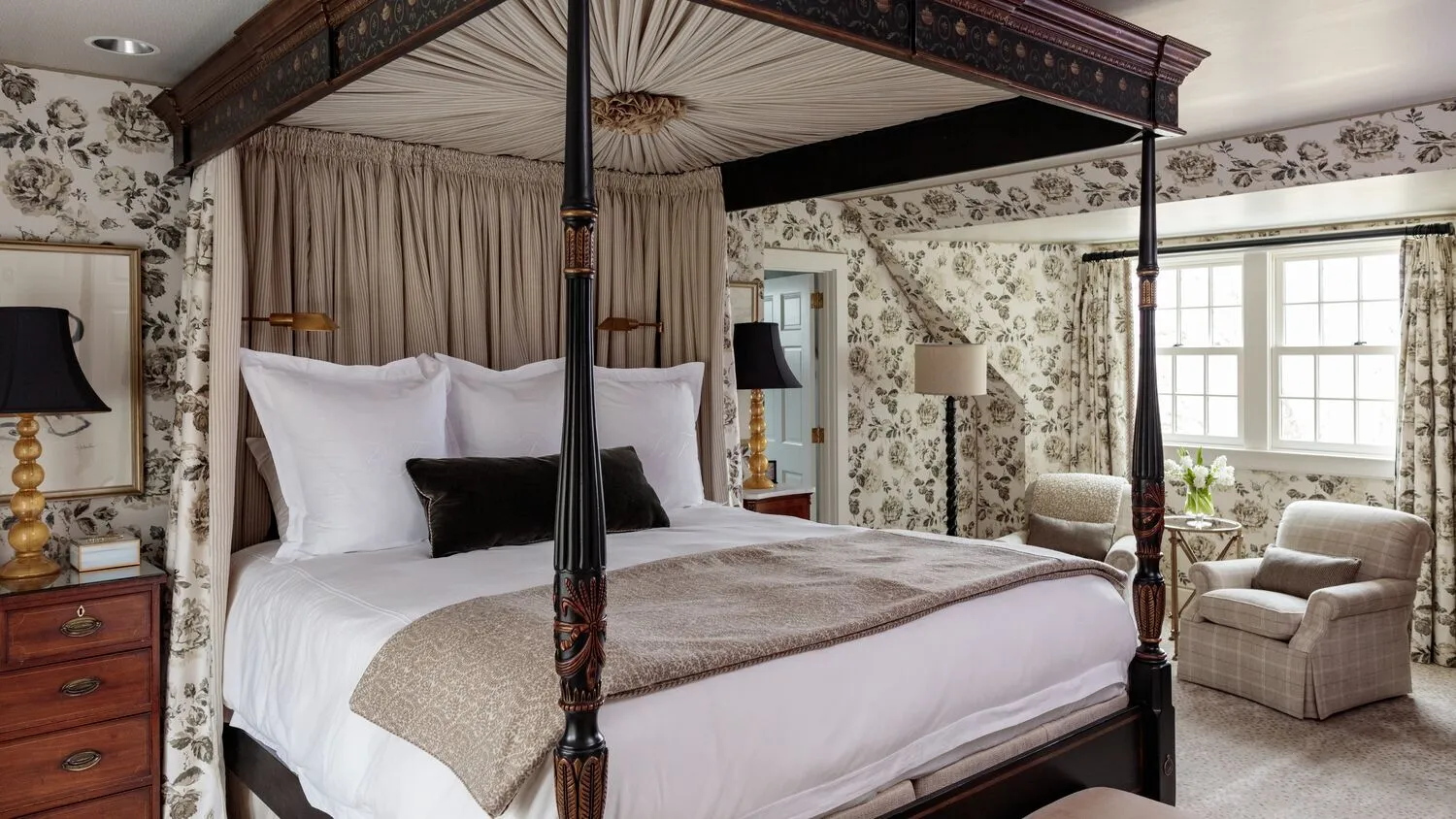 A Historic Room with a dark wooden four-poster, grey floral wallpaper and 2 armchairs by the window.
