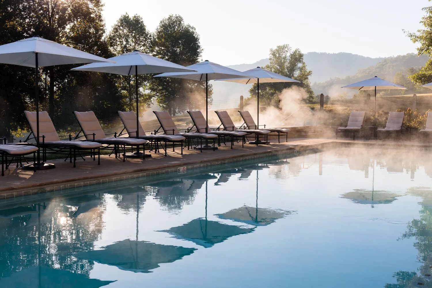 The Wellhouse pool in the morning: steam on the water, loungers under the parasols and the mountains against the light.