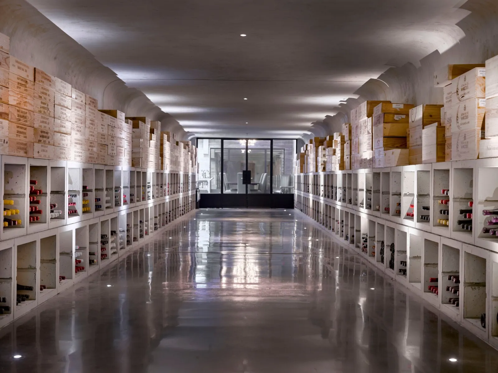 The cellar’s tunnel: a long white vaulted passage, wooden cases stacked above the racks of bottles and a polished floor.