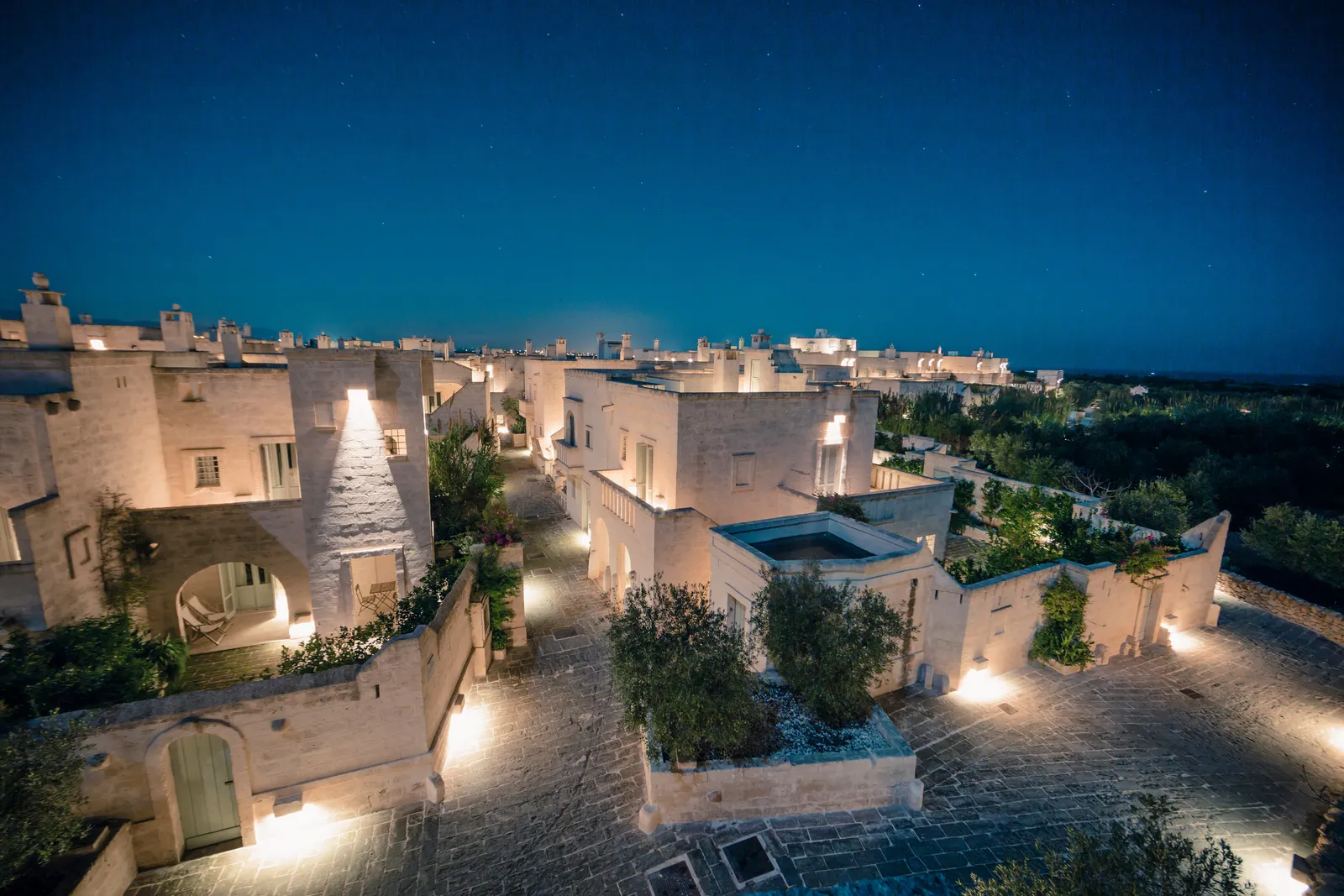 Il Borgo at night from above: stone houses with outside stairs and terraces, paved lanes lit by low lights and a few stars in the sky.