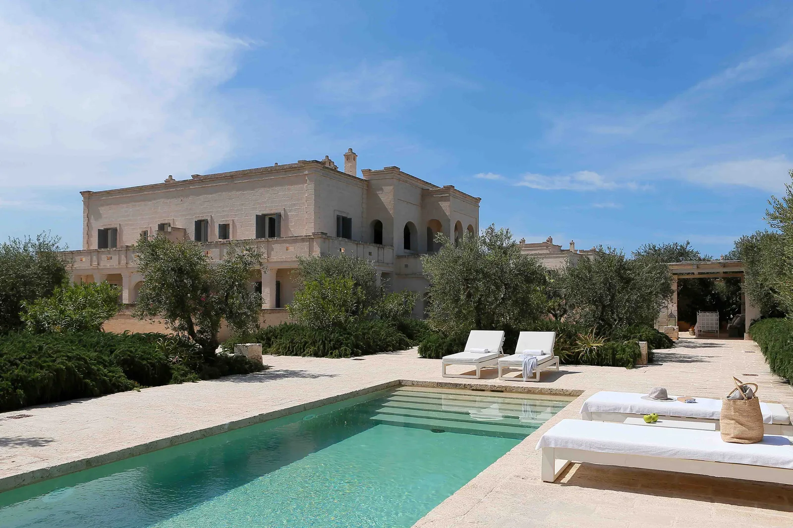 Casa Magnifica from its garden: the private pool with 2 loungers, olive trees and the 2-storey stone house.