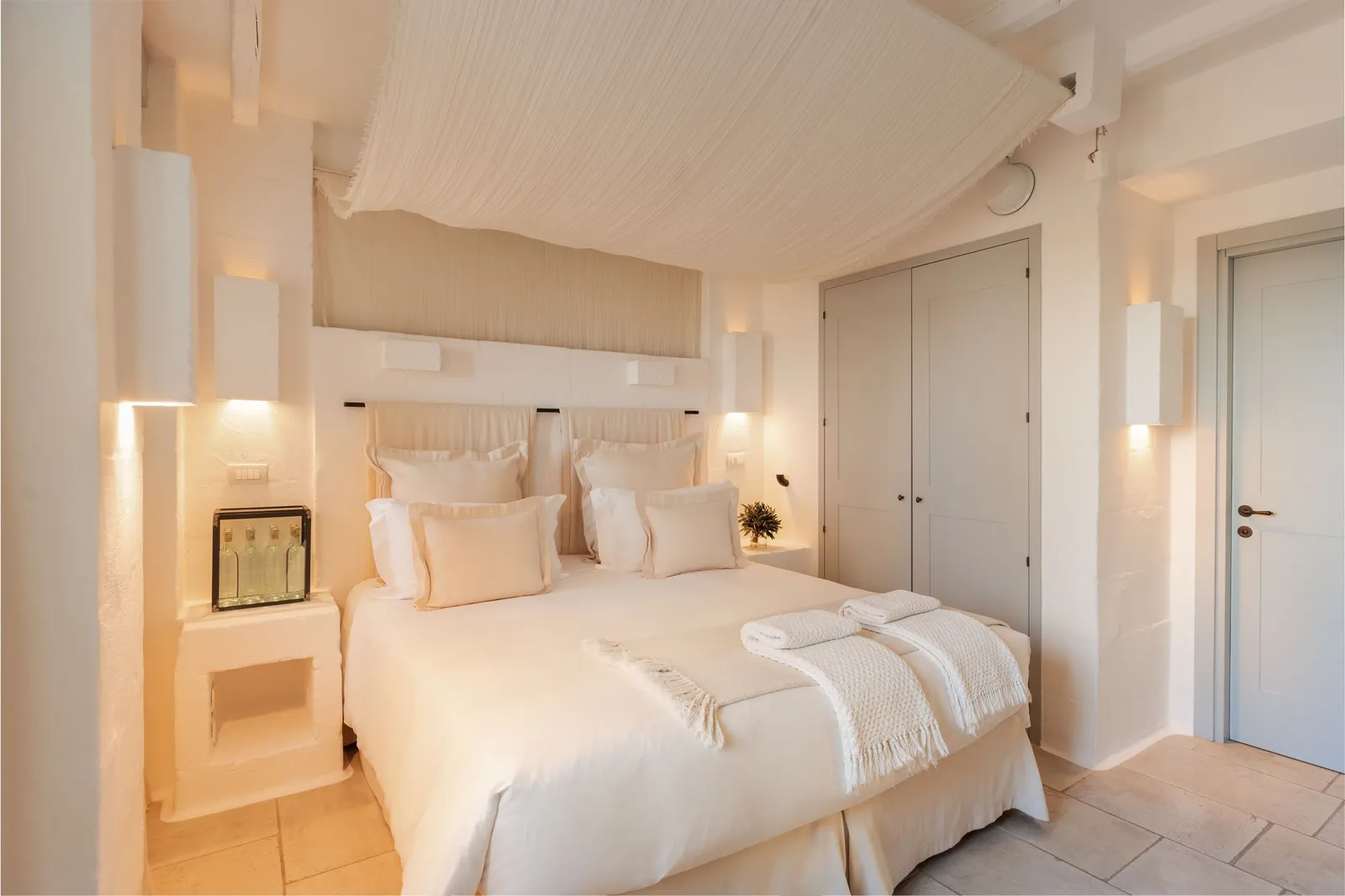 A Casetta Bella bedroom: double bed under a draped canopy, built-in bedside tables with glass lamps and a fitted wardrobe.