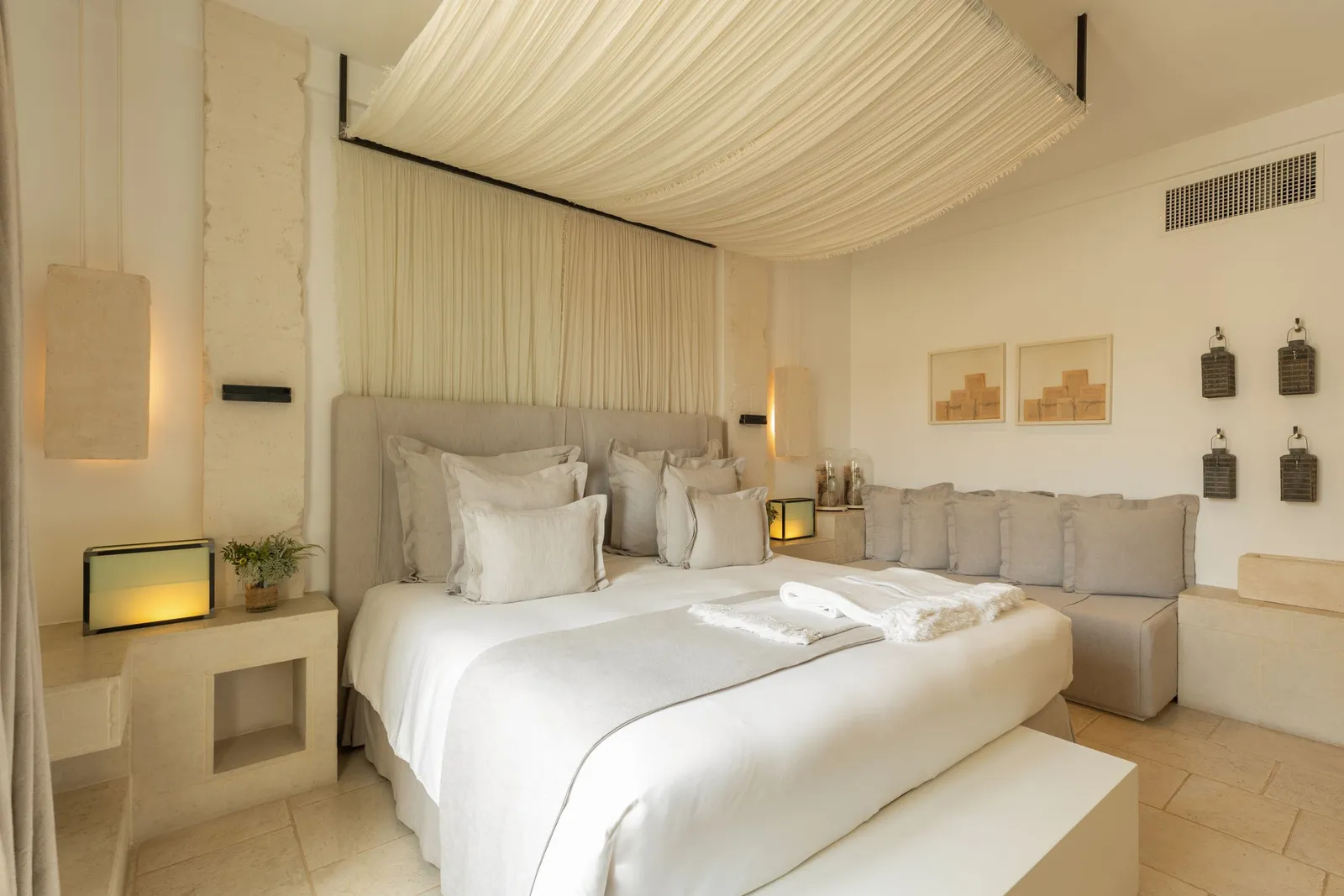 A La Corte Bella room: double bed under a draped canopy, a long sofa with grey cushions, framed prints and wall lanterns.