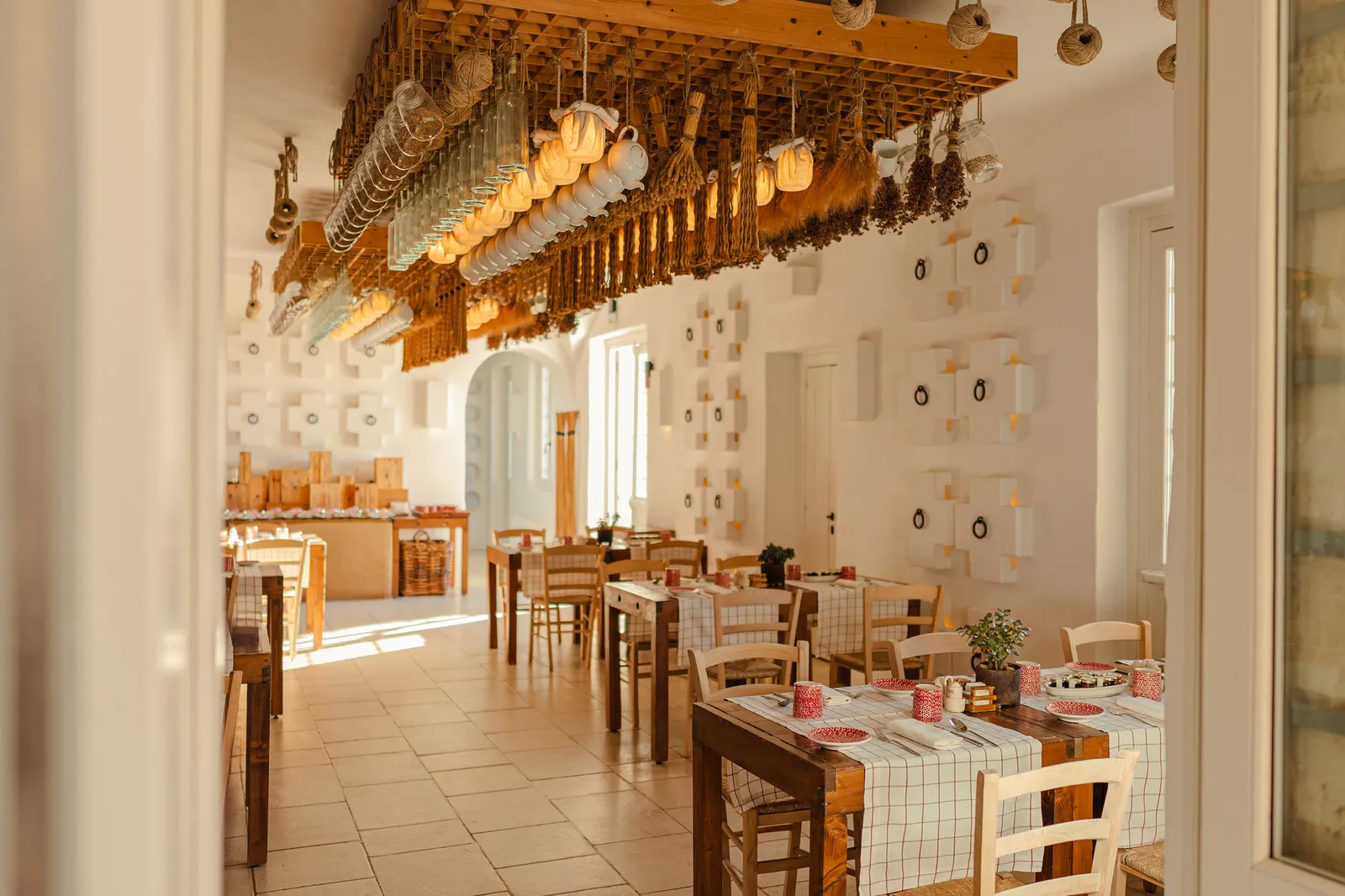 La sala della Frasca: tavoli di legno, tovaglie a quadri, erbe essiccate, tazze e bottiglie appese al soffitto.