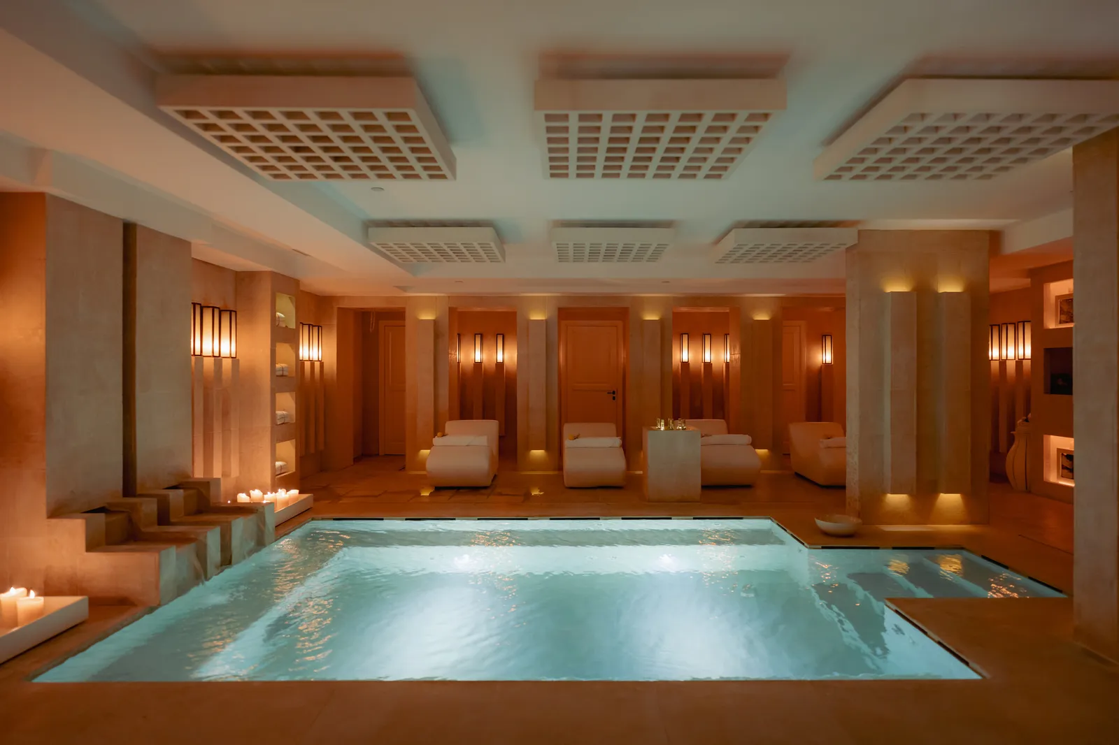 The Roman baths at Vair Spa: a lit pool with steps and candles, white loungers along the back wall and a ceiling of lattice panels.