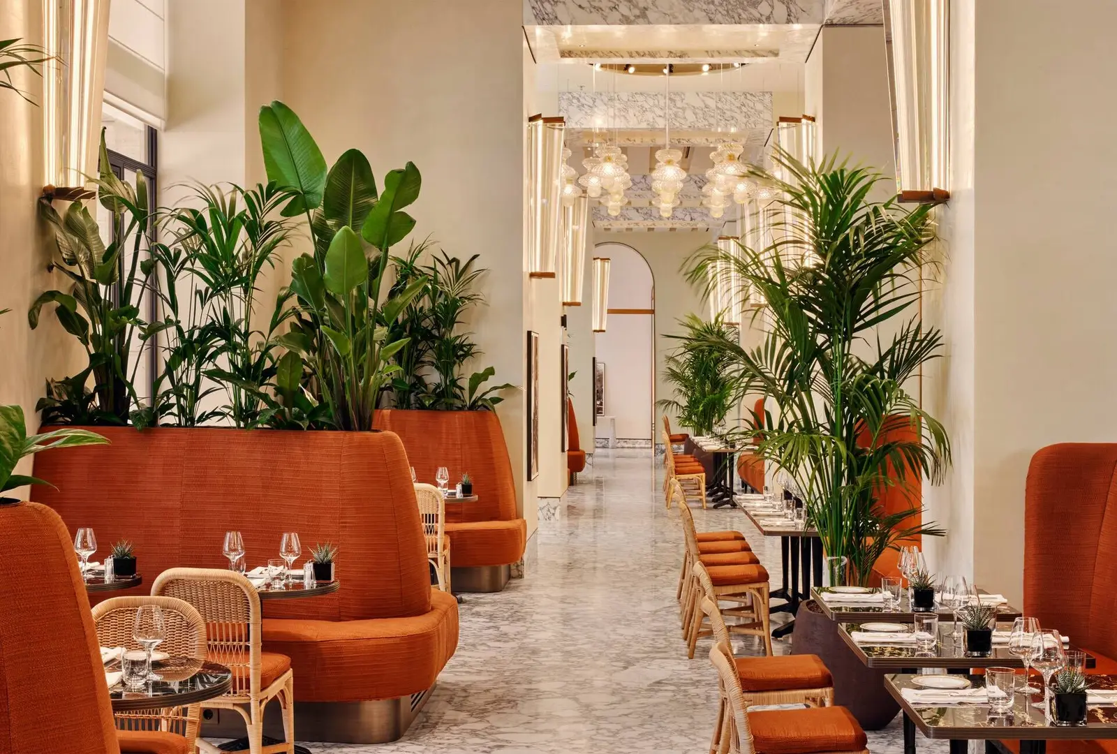 Il Caffè: terracotta-coloured banquettes and rattan chairs, laid tables, potted palms and plants, a marble floor and glass pendant lamps down the room