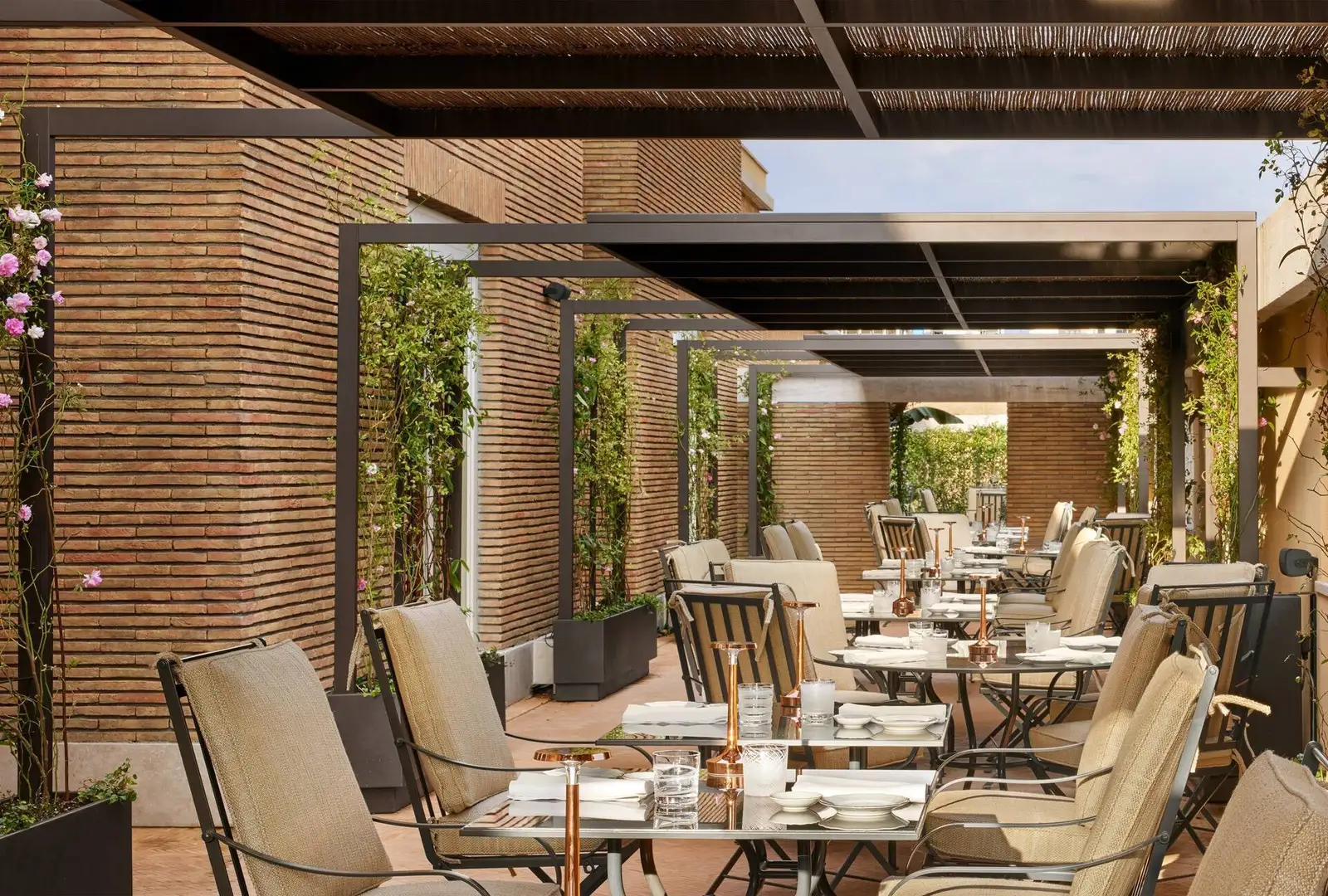 Il Ristorante’s terrace: tables laid with copper lamps under a reed-covered pergola, brick walls with climbing roses and iron chairs with sand-coloured cushions