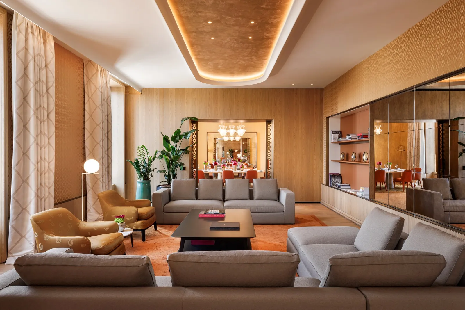 The Bvlgari Suite living room: grey sofas and armchairs round a low table, wood panelling and a lit ceiling cove