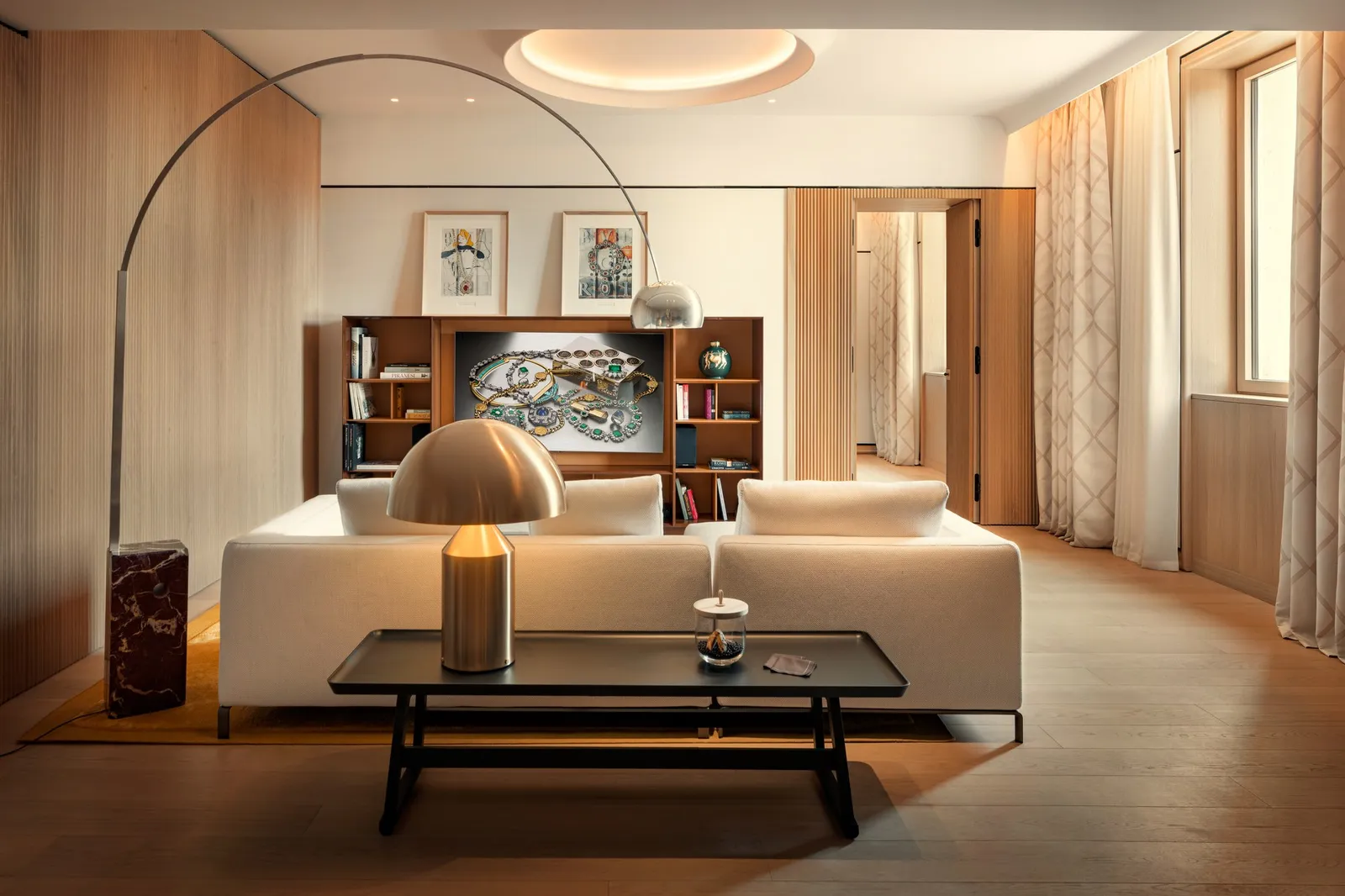 A Deluxe Suite living room: a long white sofa under an arc lamp, a low table and a bookcase with a painting