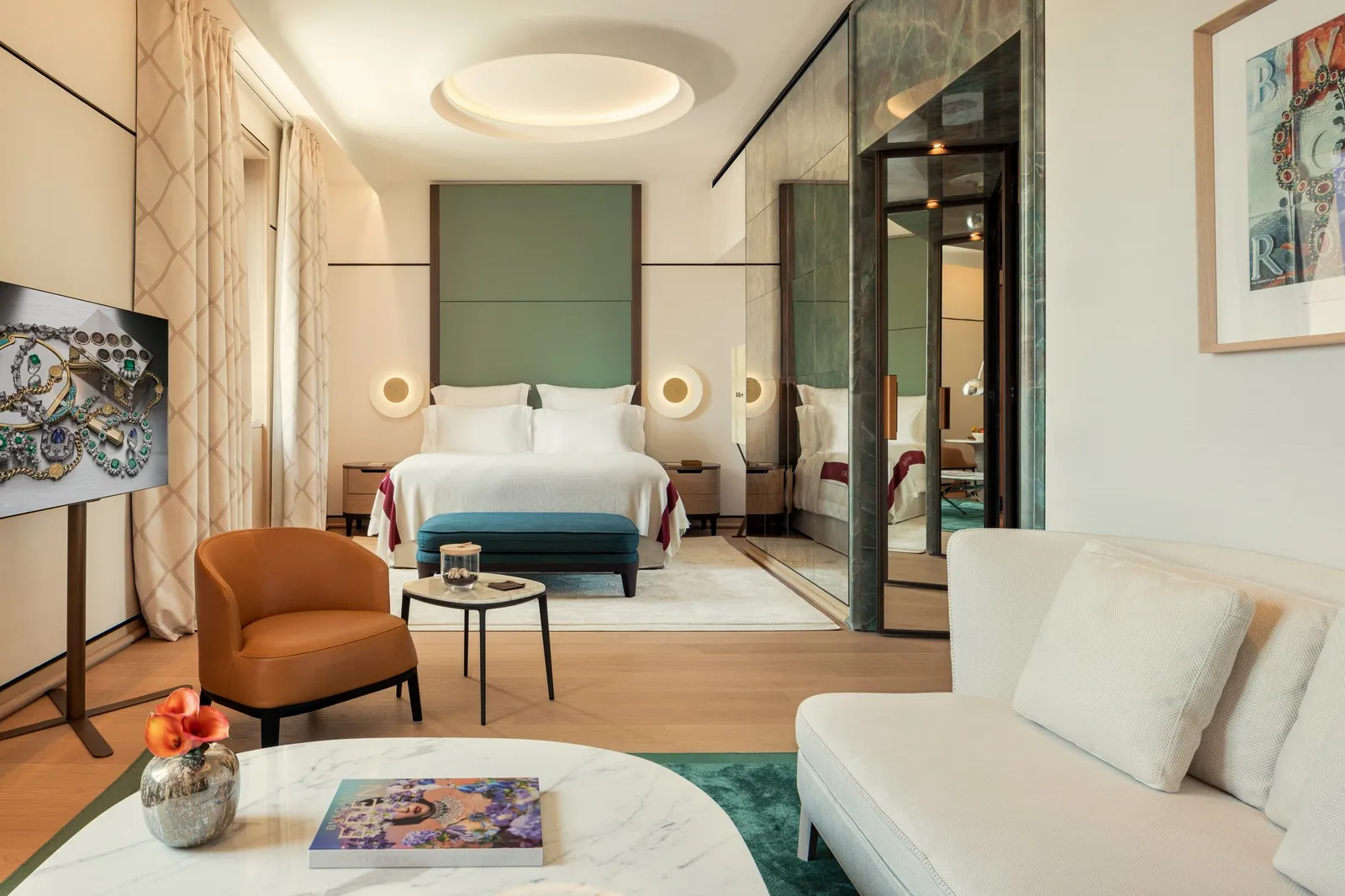 A Junior Suite: an armchair and a white sofa in the sitting area, and the bed under a green headboard beyond