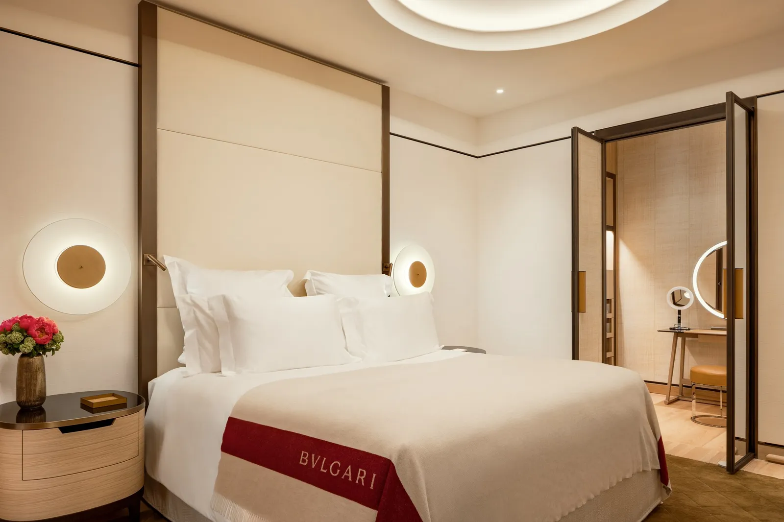 A Premium Room: a bed with a tall cream headboard, a round wall lamp and the dressing area beyond a glass door
