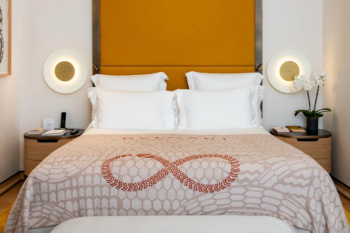 The Serpenti Suite bedroom: a bed with a throw patterned like serpent scales, under a mustard headboard