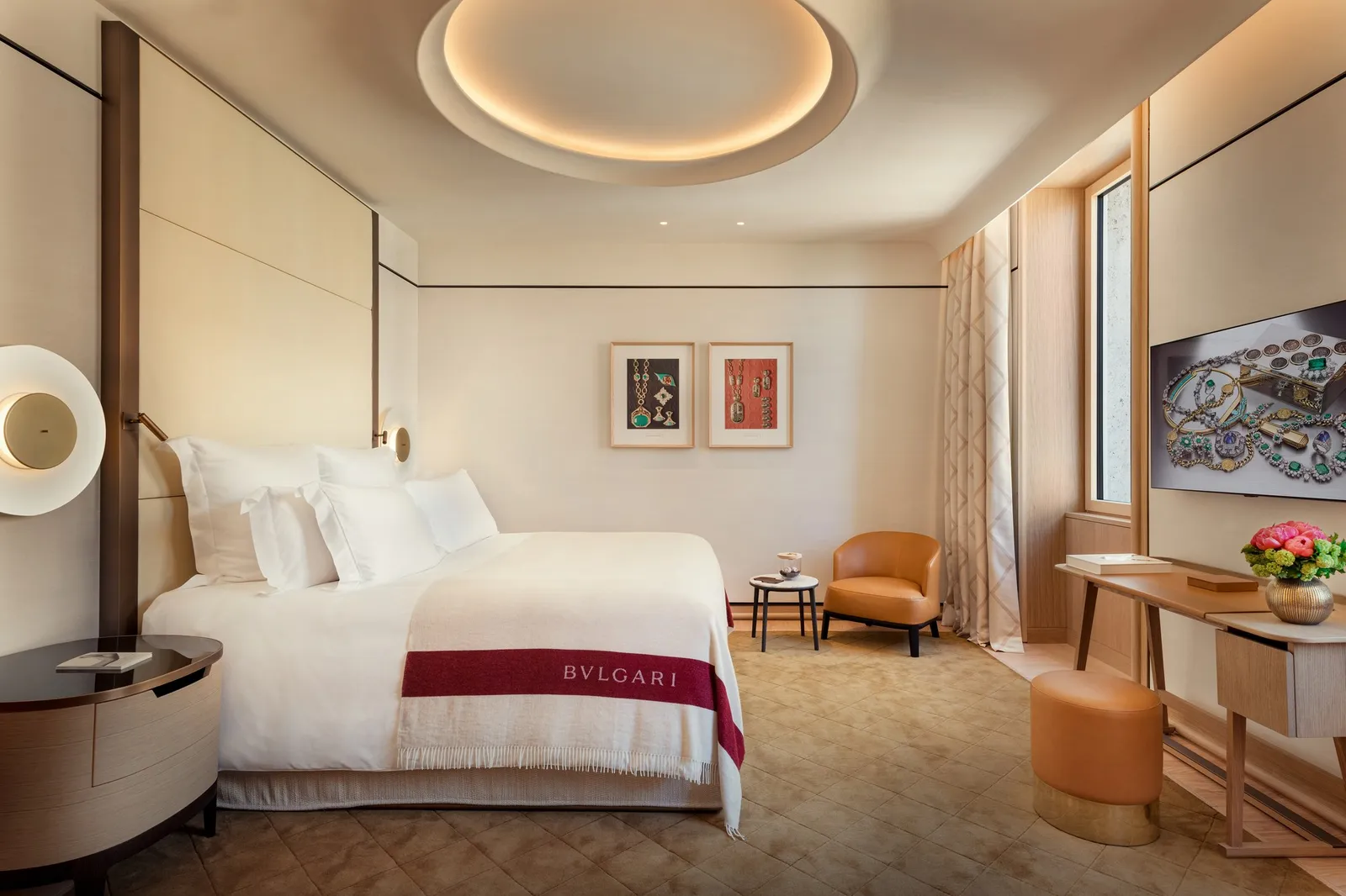 A Superior Room: a bed with a red Bvlgari throw, framed prints, a leather armchair and a desk by the window