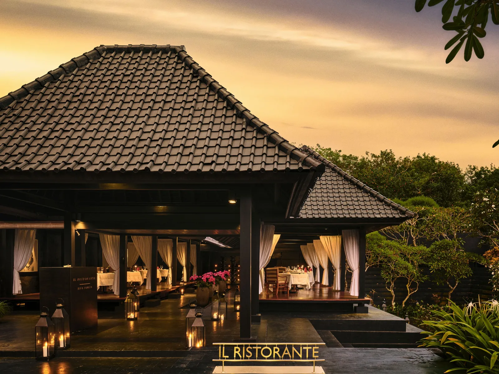 Il Ristorante at dusk: the pavilion under its steep roof open to the evening, laid tables, candles and the Il Ristorante sign.