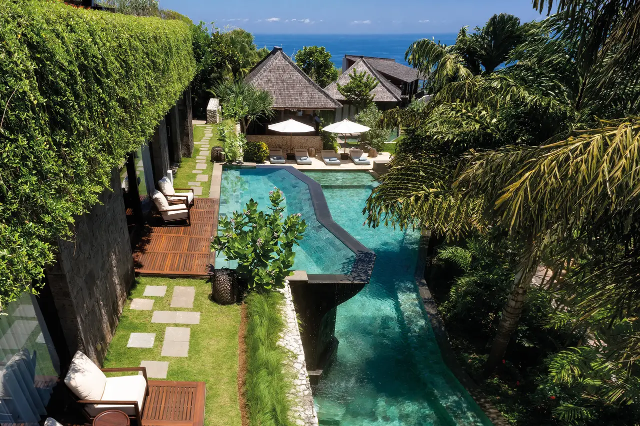 A Mansion’s 2-tier pool from above: the stepping-stone path on the lawn, the loungers and the sea beyond the roofs.