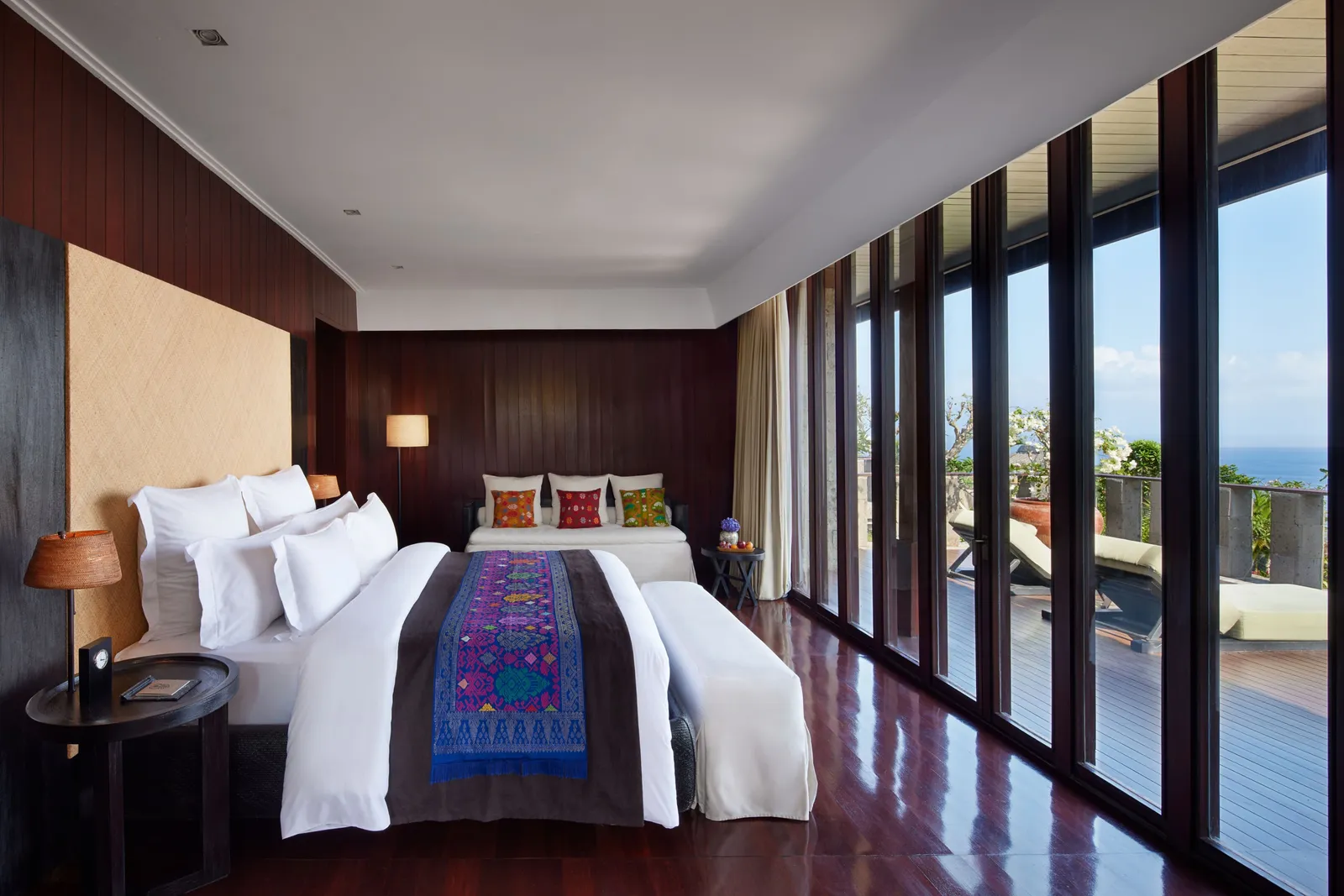 A bedroom of the Bvlgari Villa: the bed with its blue runner, floor-to-ceiling glass onto the terrace.