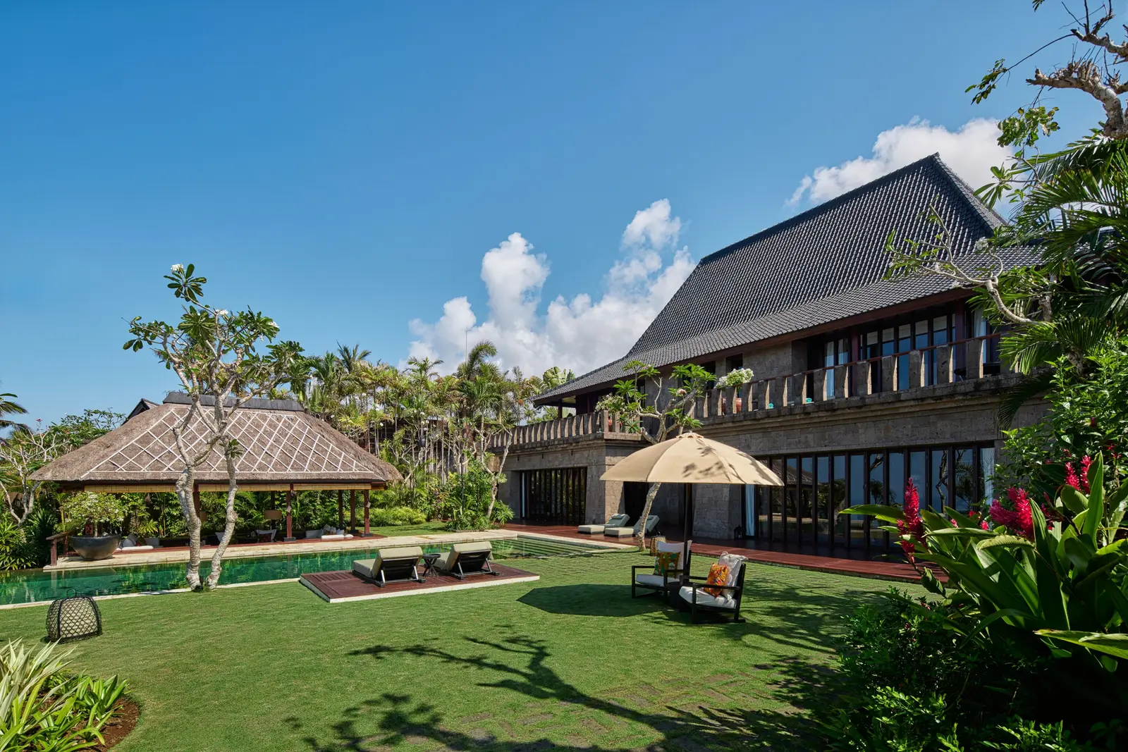 The Bvlgari Villa from the lawn: the 2-storey stone house, a thatched pavilion and the parasol.