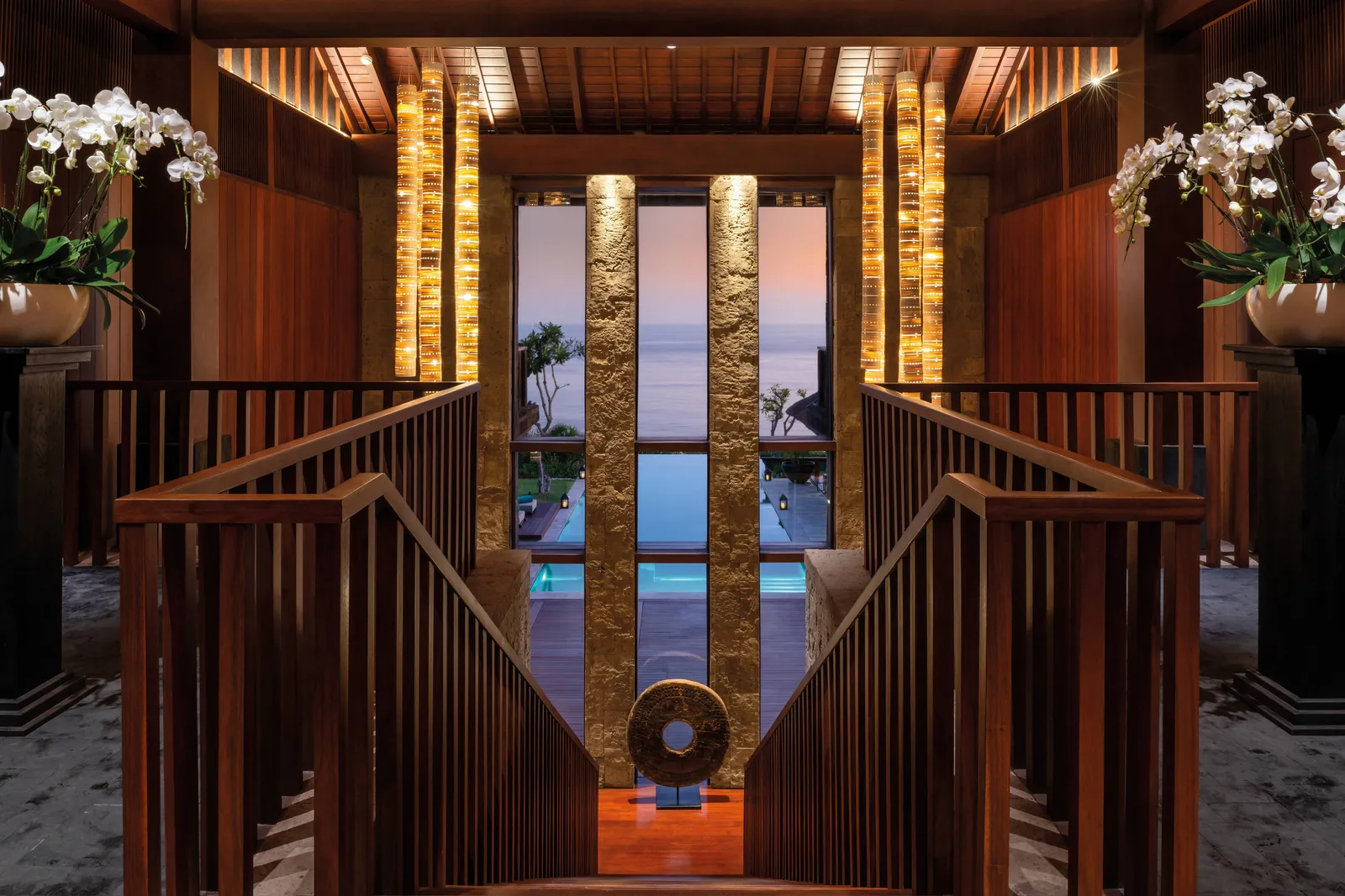 The double staircase of the Bvlgari Villa running down towards the pool, between white orchids and lit stone pillars.