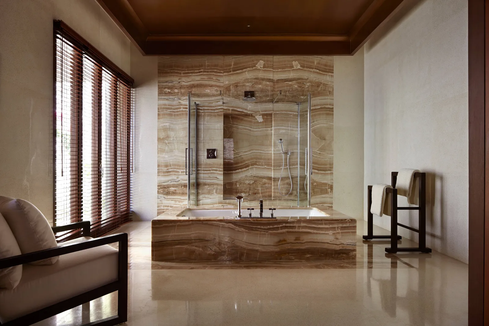 A Mansion bathroom: the tub clad in veined marble, the glass shower and the wooden shutters.