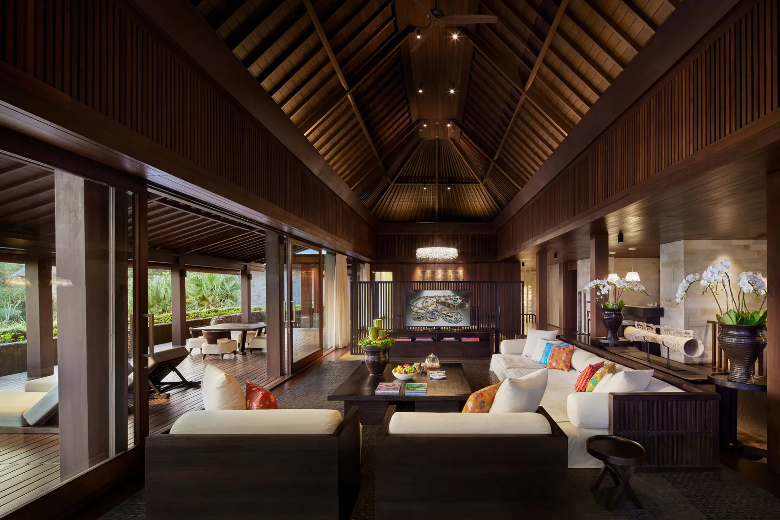 A Mansion living room: white sofas and orchids under the tall timber roof, the dining room beyond.