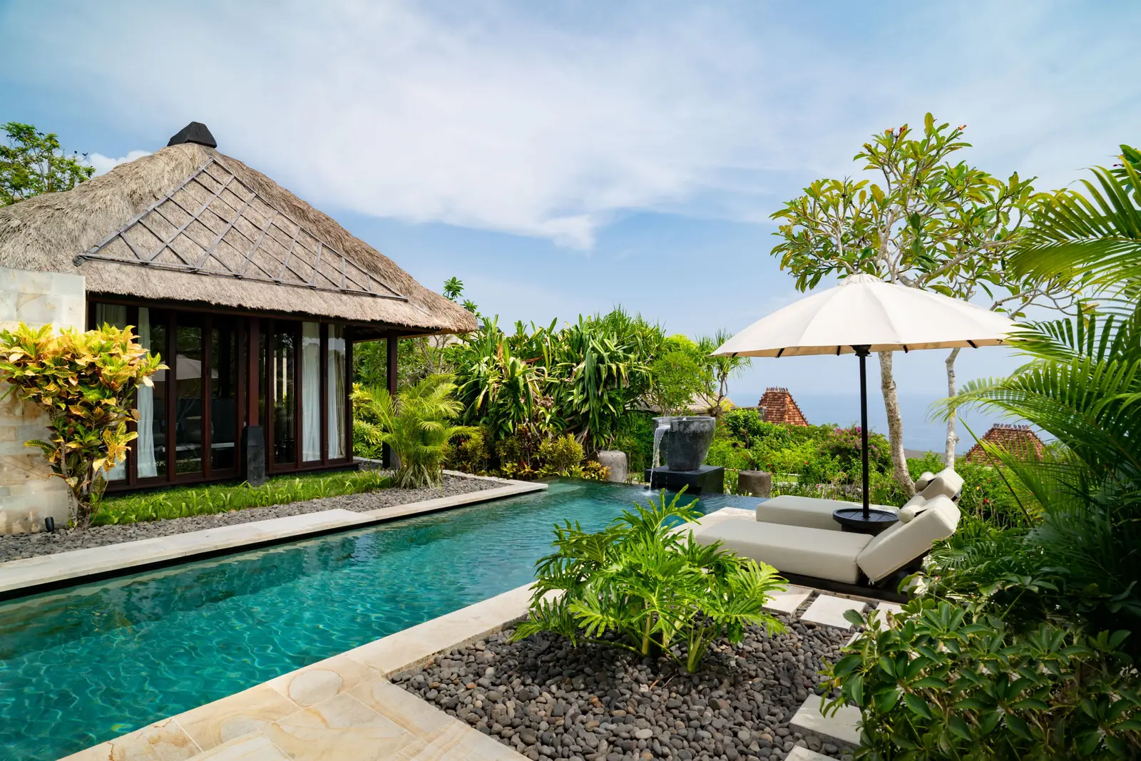 A 2-bedroom villa’s pool among the plants, the thatched pavilion and a lounger under the parasol.