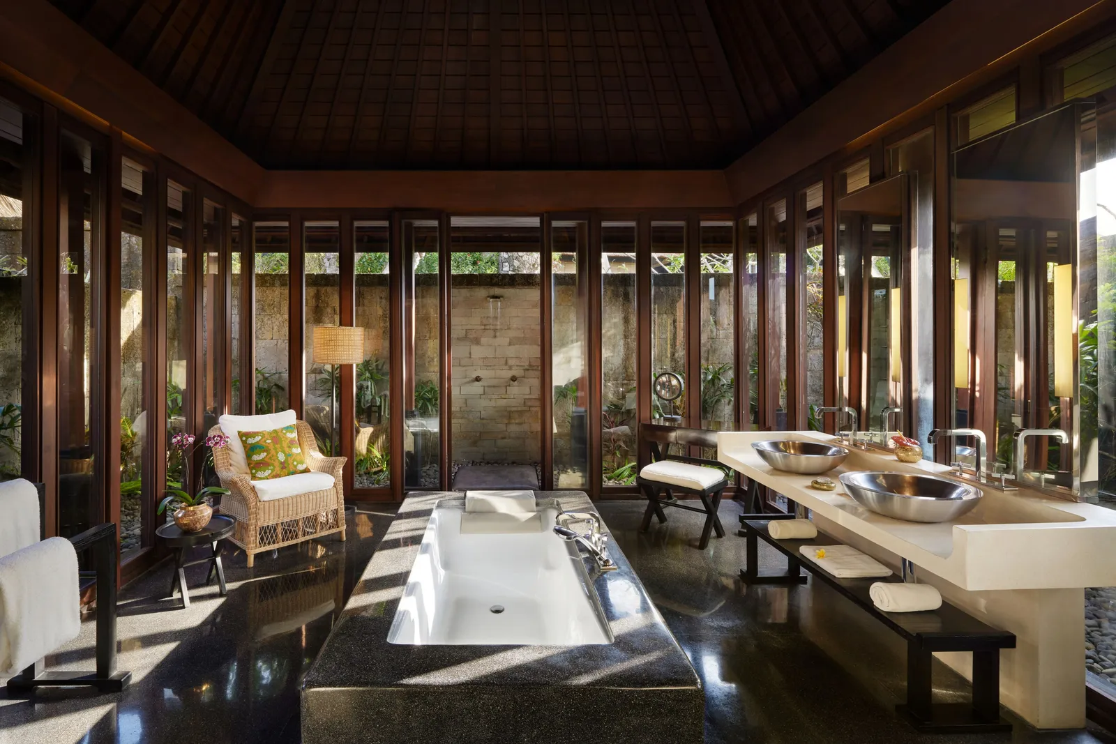 A villa bathroom: the tub set into the terrazzo floor, the double basin and the glass walls onto the walled garden.