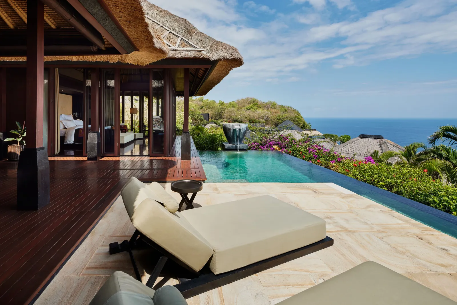A Premier Ocean View Villa: loungers on the stone deck, the infinity pool and the sea beyond the thatched roofs.