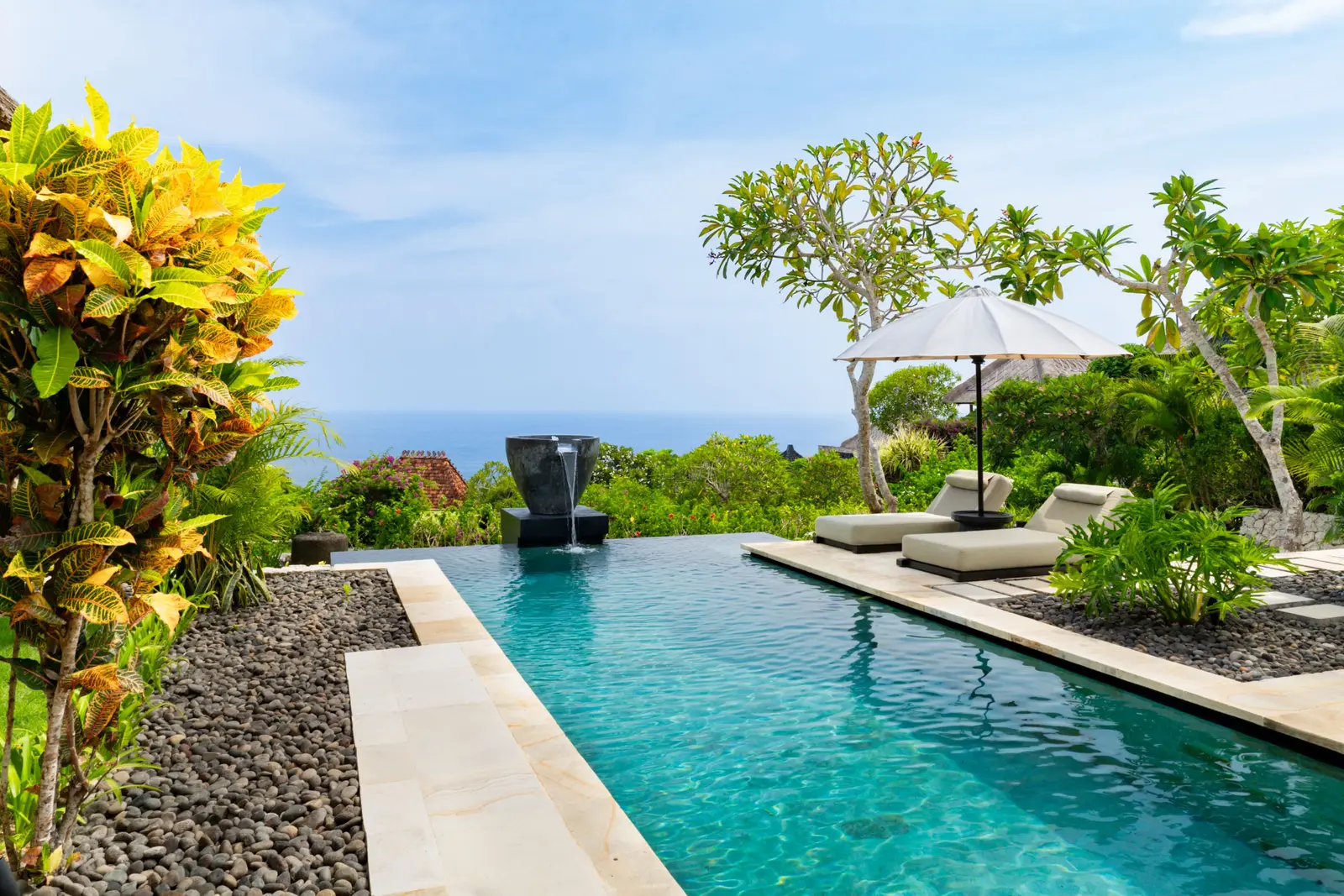 The pool of a 2-bedroom Premier Ocean View Villa, between pebbles and crotons, with the loungers and the sea at the end.