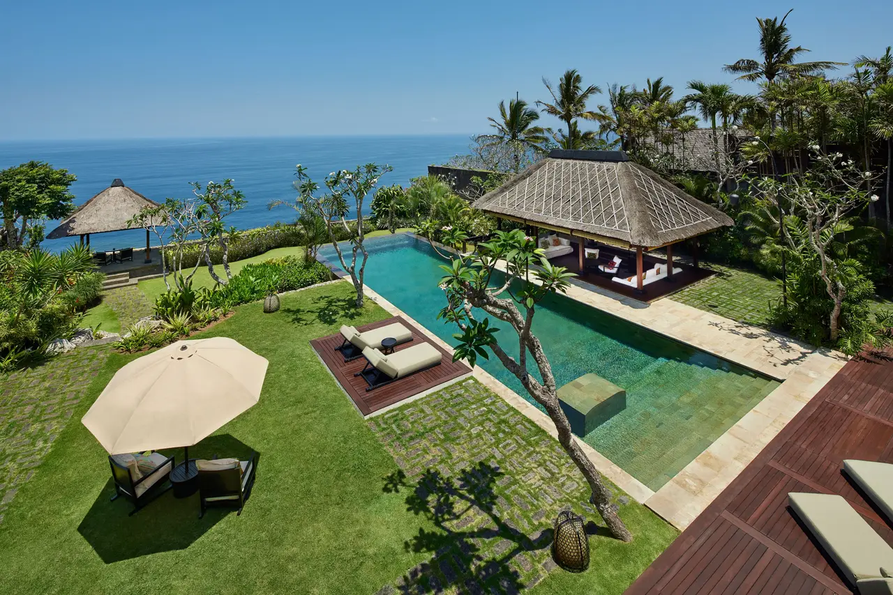 The Bvlgari Villa from above: the long pool on the lawn, a thatched pavilion, loungers under a parasol and the ocean behind.
