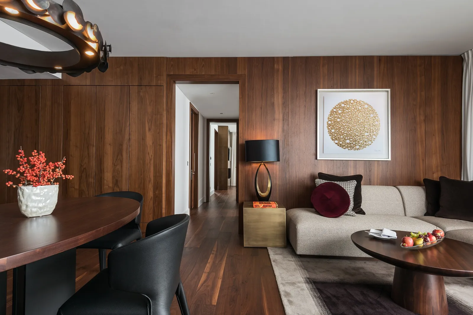 The living room of a Contemporary Family Suite: walnut panelling, a sofa, a round table and a corridor to the second bedroom