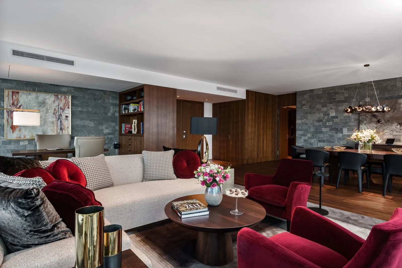 The living room of the Penthouse Suite: red velvet armchairs, a long sofa, stone walls, bookshelves and a dining table